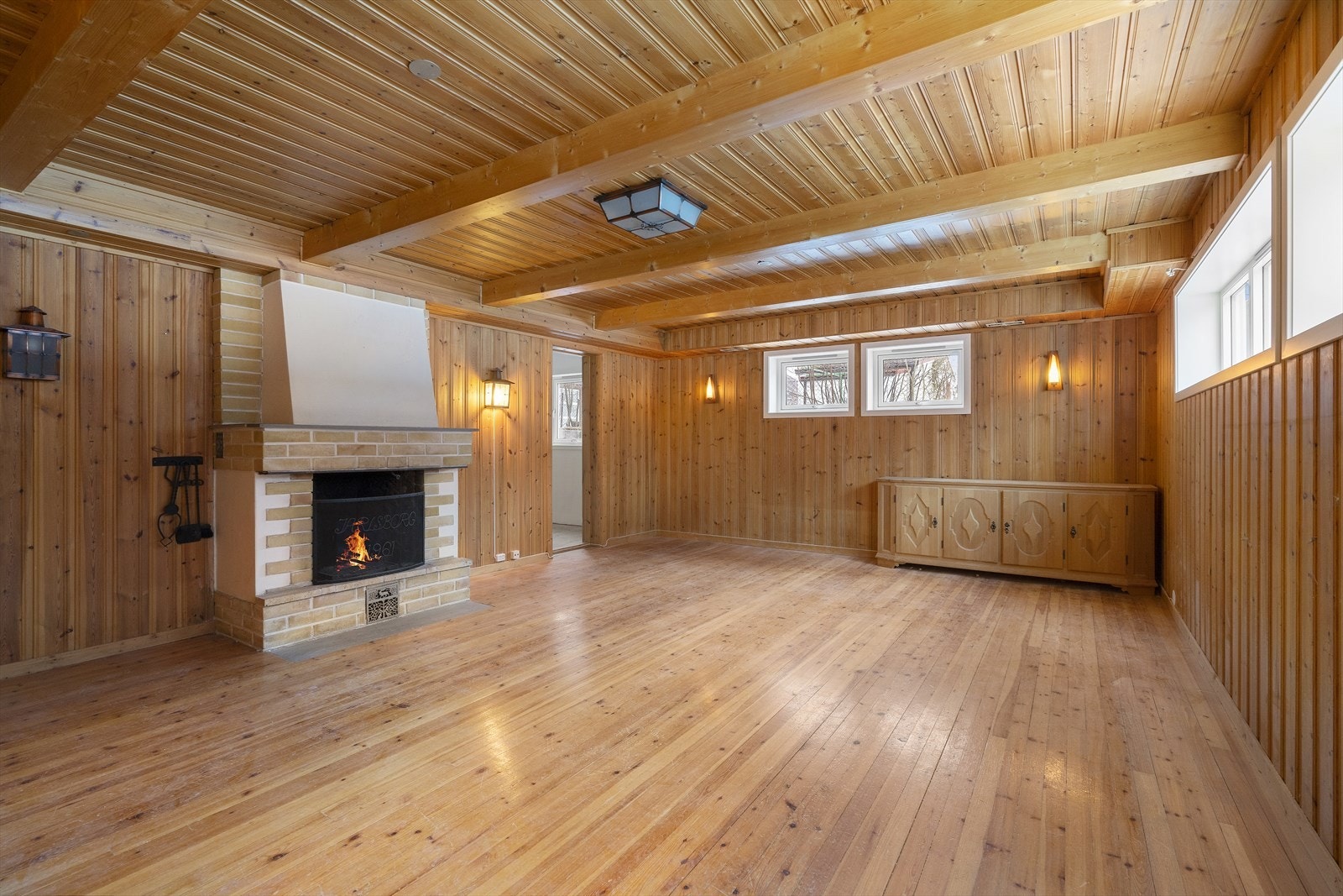 Kjellerstue med peis og murt teglsteinspipe. I enden av rommet har man tilgang til et av sokkeletasjens soverom. Galleribilde