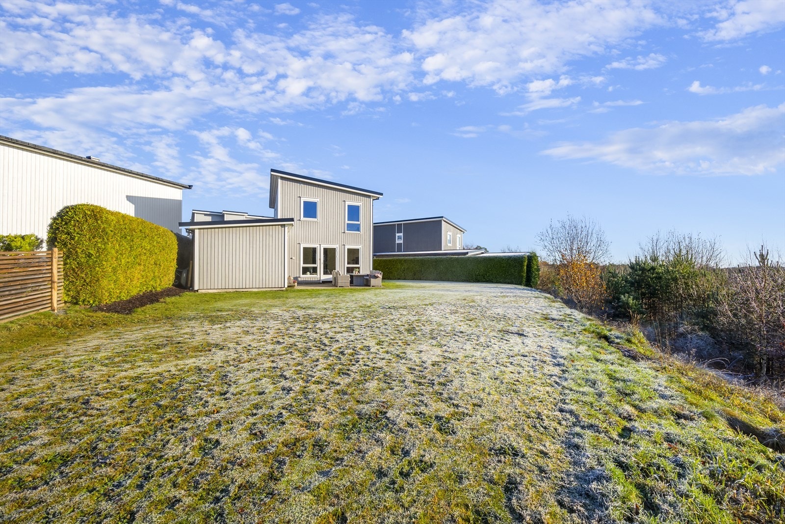 Relativt flatt terreng rundt boligen er opparbeidet med plen og belegningsstein. Fasaden har stående bordkledning som gir et ryddig utseende. Boligen grenser til friområde i boligfeltet tilhørende Arendal Kommune. Galleribilde