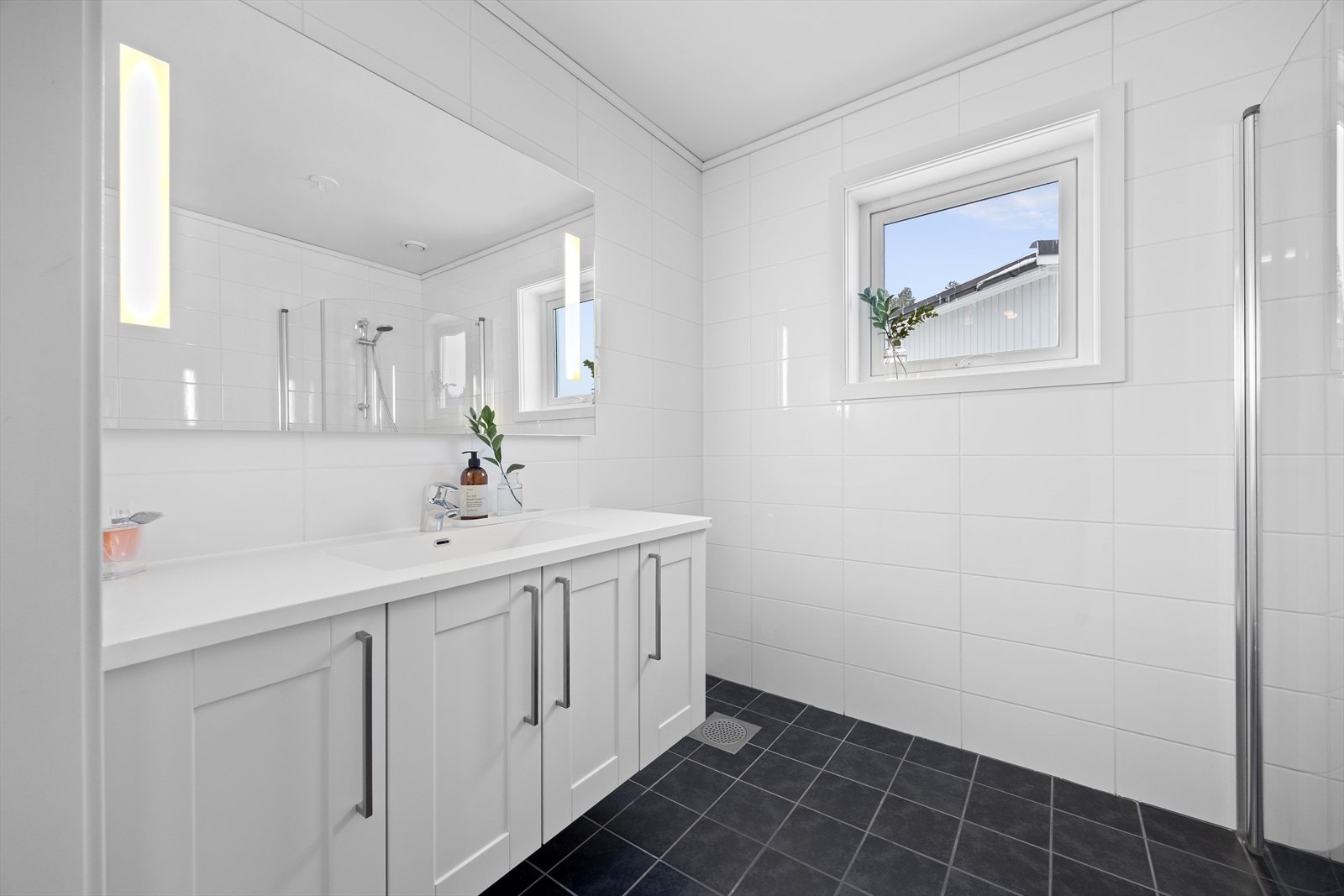 Romslig, flislagt bad med varmekabler i gulv. Badet er innredet med dusj, hvit baderomsinnredning med speil og skal, toalett, samt opplegg til badekar. Galleribilde