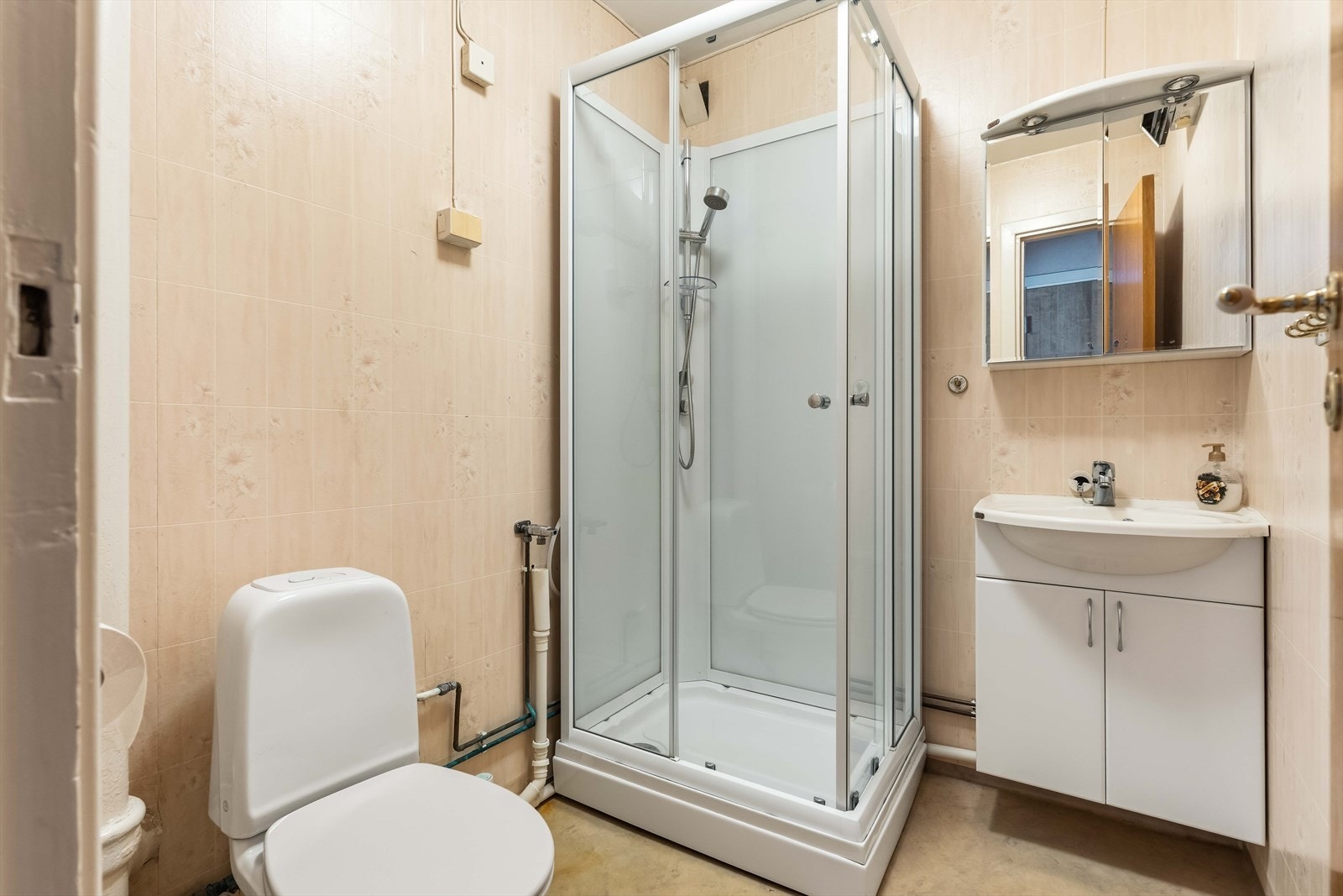 Badet har belegg på gulv og tapet på vegg. Innredningen består av et servantskap med toppmontert servant og ettgreps blandebatteri. Dusjkabinett og toalett. Galleribilde