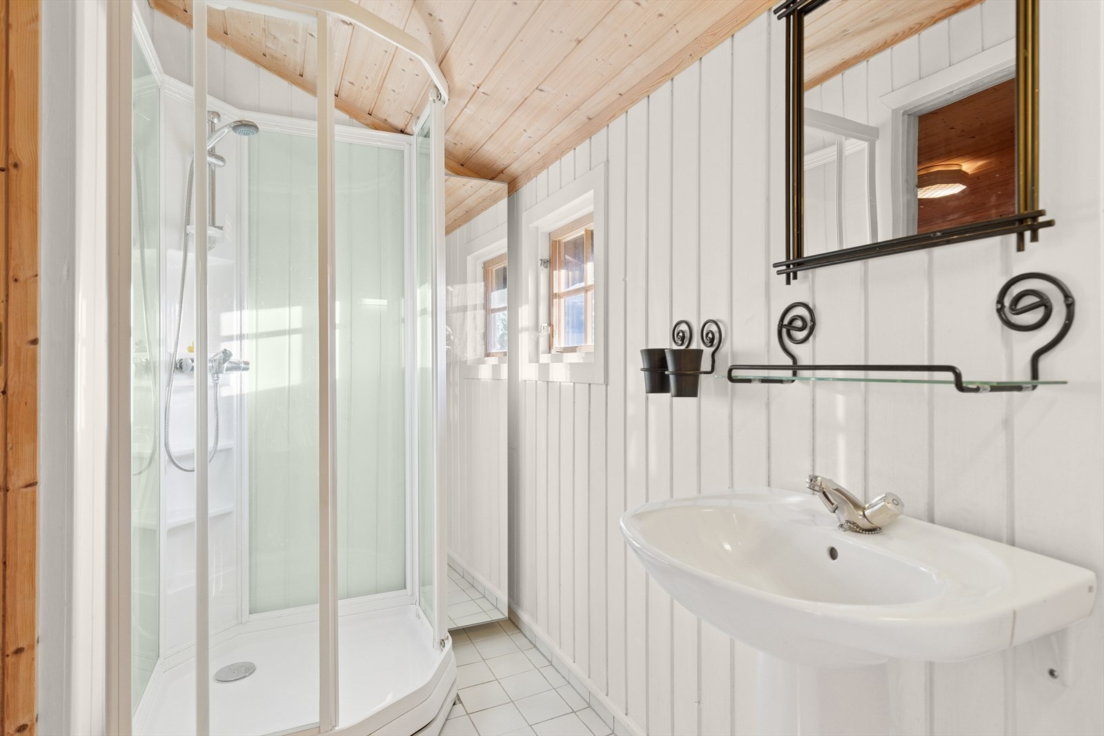 Bad med panel på vegger og fliser på gulv. Badet er innredet med servant og dusjkabinett. Galleribilde