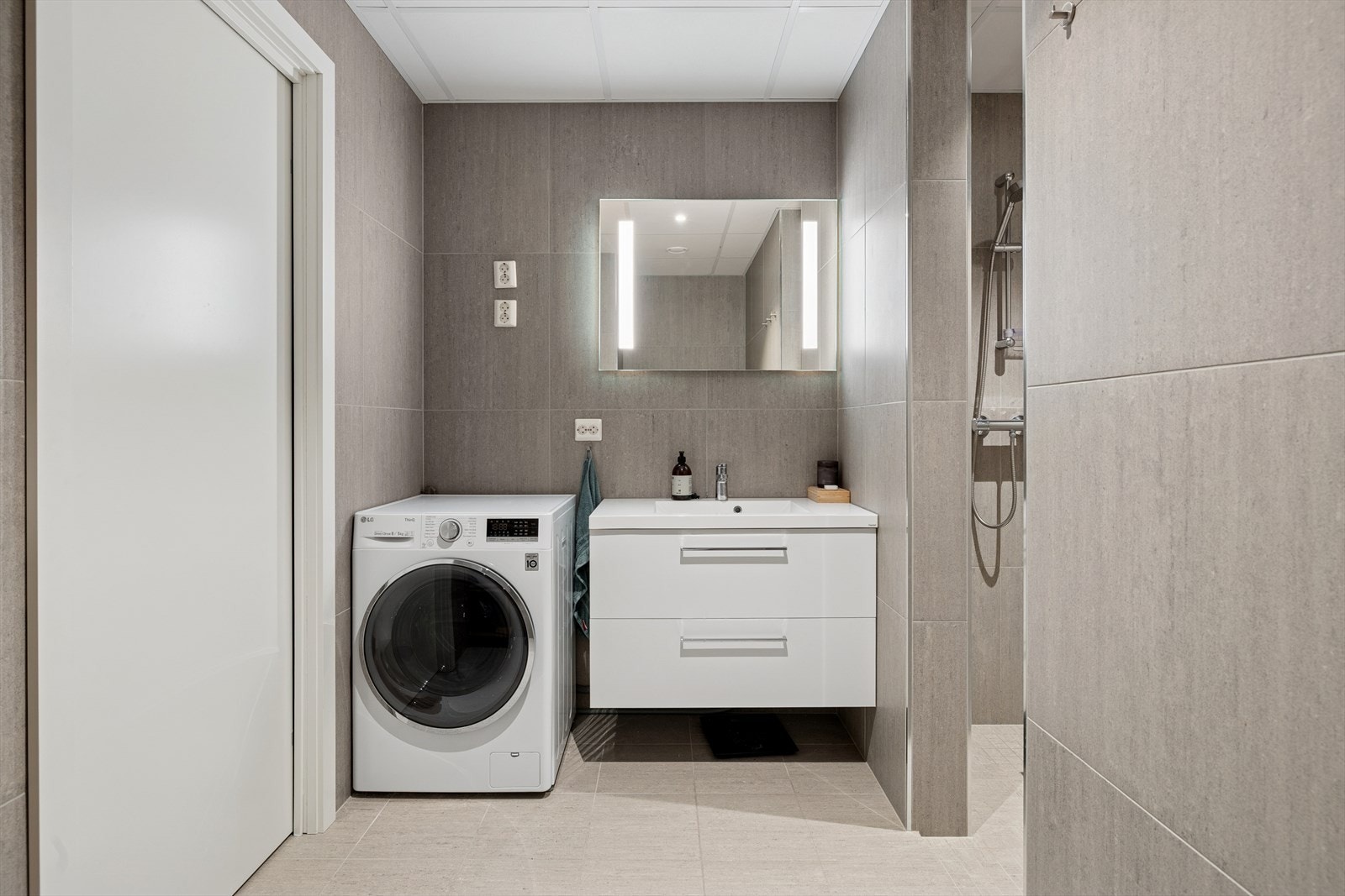 Innredning med skuffer og heldekkende servant, speil med intergrert belysning, vegghengt toalett, dusjnisje og opplegg for vaskemaskin. Galleribilde