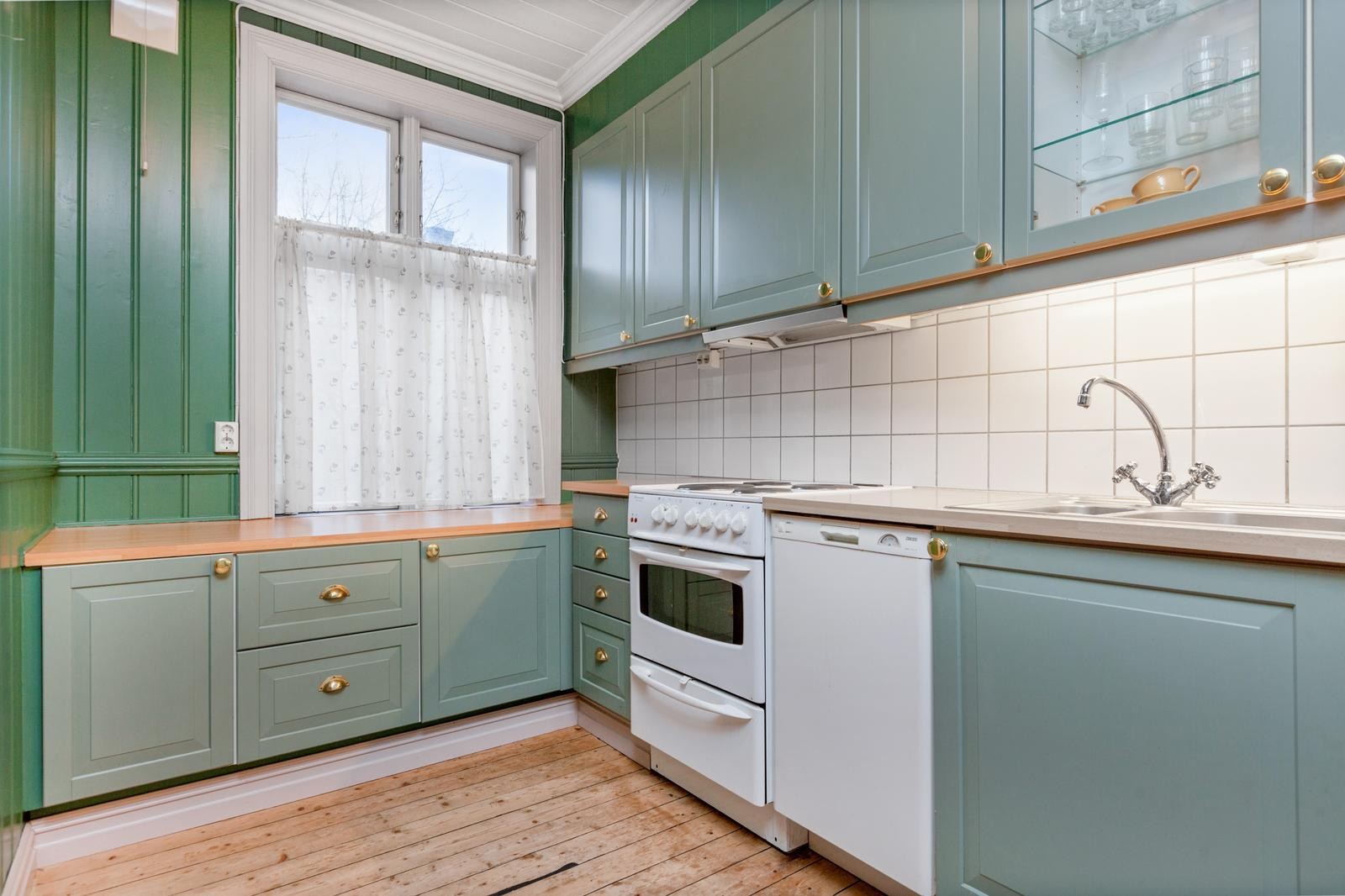 Stilrent kjøkken med hvitevarer som oppvaskmaskin, komfyr og kjøleskap. Galleribilde