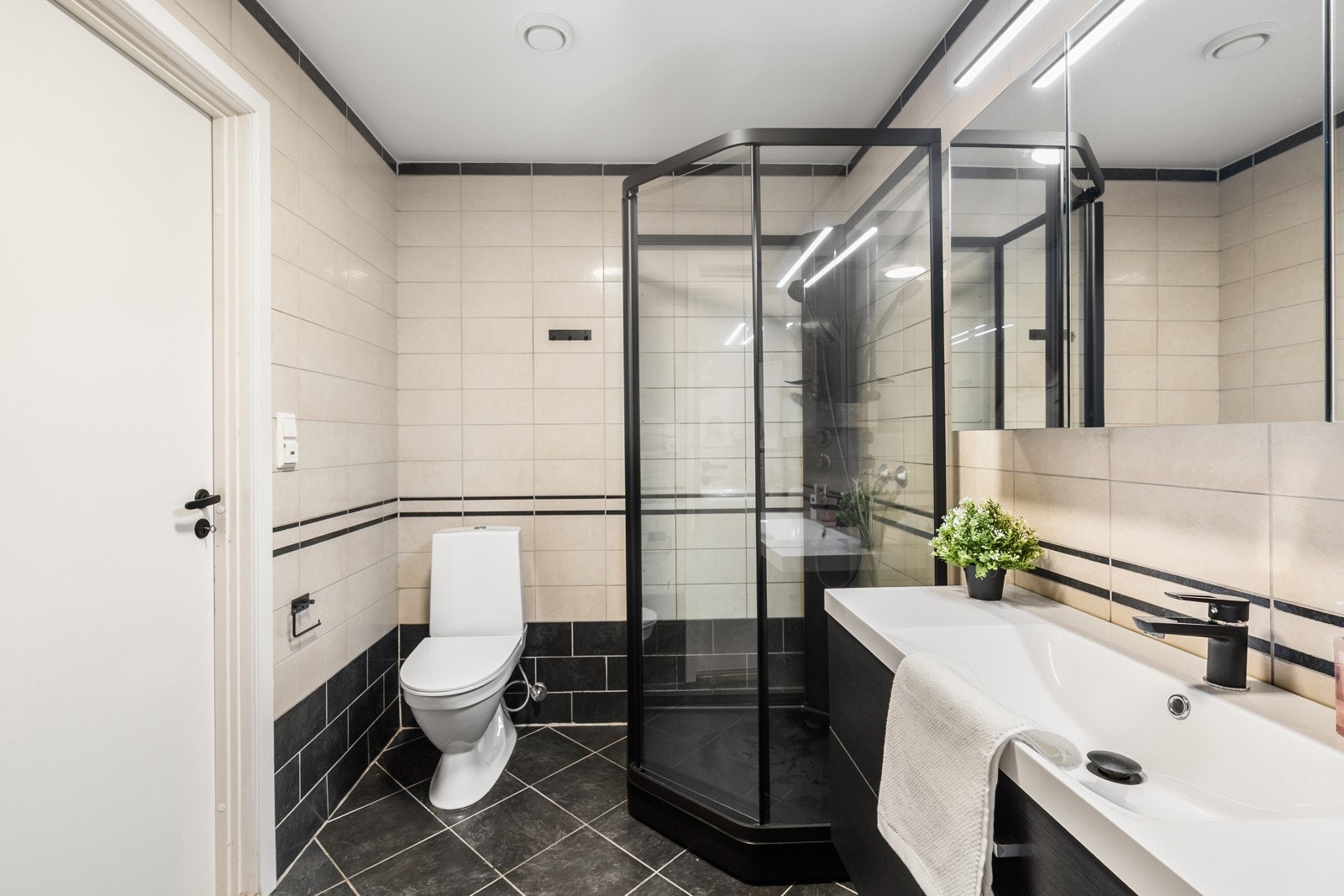 Baderomsinnredningen består av seksjon med helservant, speil med belysning, dusjkabinett, og gulvstående toalett. Galleribilde