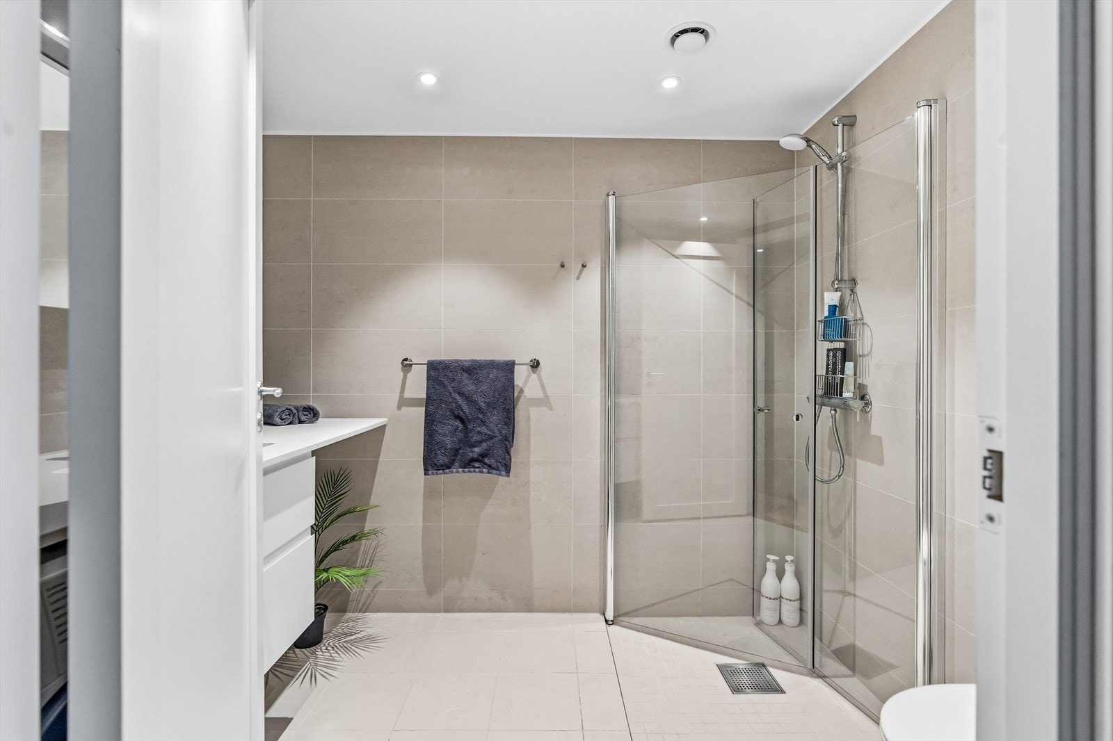 På badet er gulv og vegger flislagte. Rommet er utstyrt med dusj på gulv med dører i herdet glass, veggfestet klosett med innebygget sisterne og servant. Galleribilde