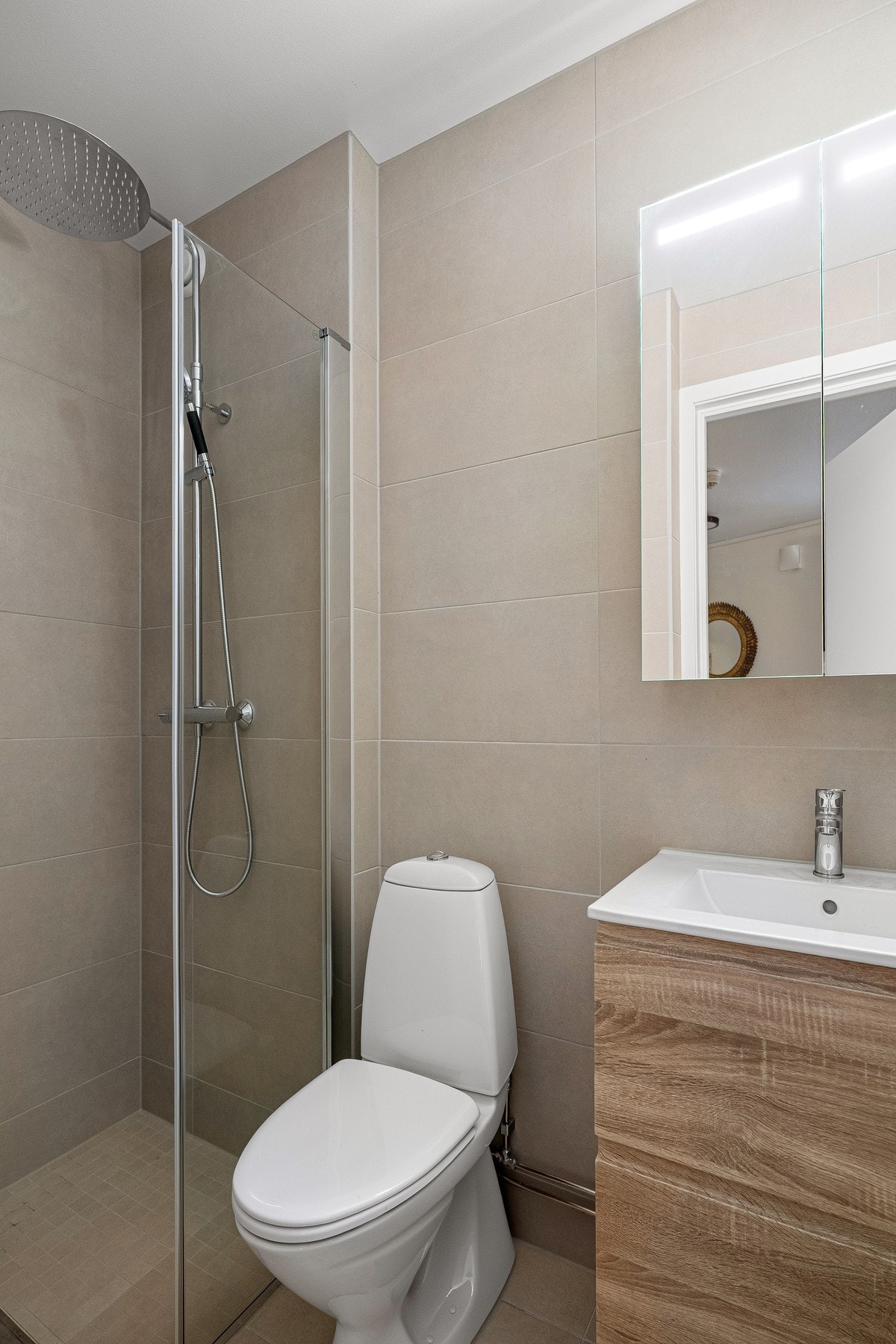 Stilren innredning med servantskap i treverk og speilskap med belysning. Galleribilde