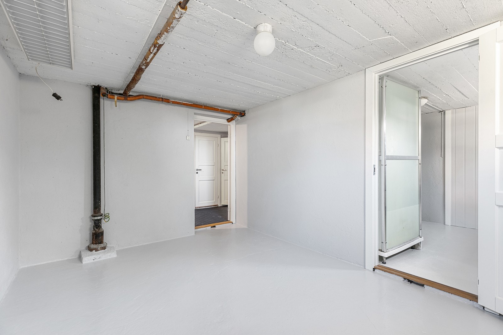 Rommet har malte vegger og tak med synlige rørinstallasjoner, og det er en enkel belysning montert. Galleribilde