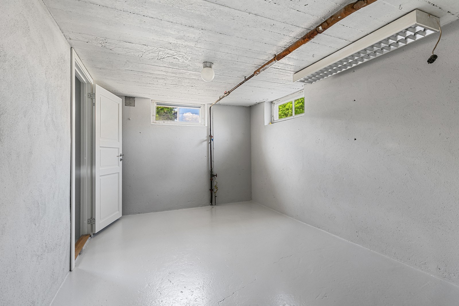 To små vinduer gir naturlig lys til rommet, som har malte betongvegger og synlige rørledninger. Galleribilde