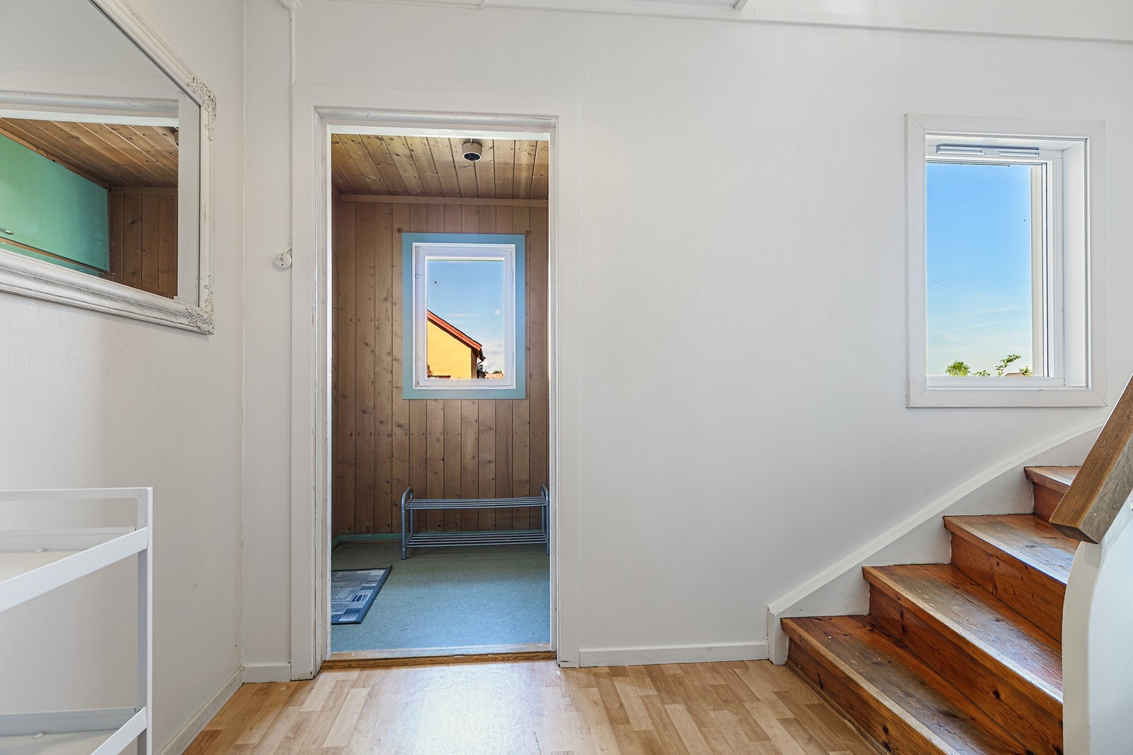 Koselig adkomst via entrè, til mellomgang med lakkert tretrapp som gir tilgang til andre etasje, med malte vegger og vindu. Galleribilde