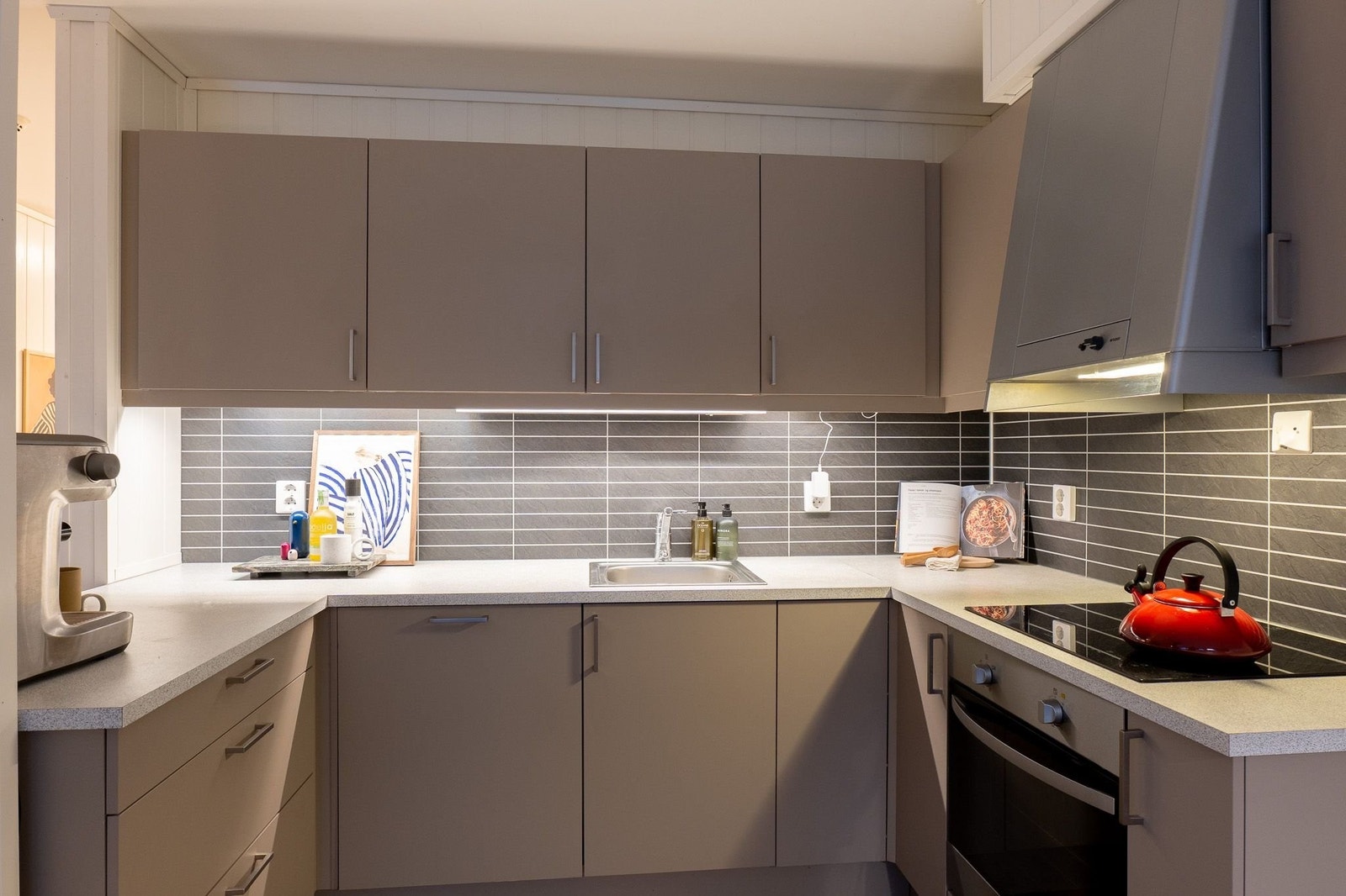 Tidløst og funksjonelt. Kjøkkenet har en stilsikker innredning med slette fronter i en behagelig gråtone. De mørke flisene over benken gir rommet karakter og er lette å holde rene. Her er plassen godt utnyttet med rikelig med skap-plass. Galleribilde