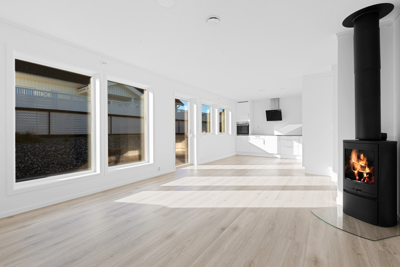 Stue med enstavs laminatgulv og malte gipsvegger. Stålpipe med hvit vedovn type Contura Galleribilde