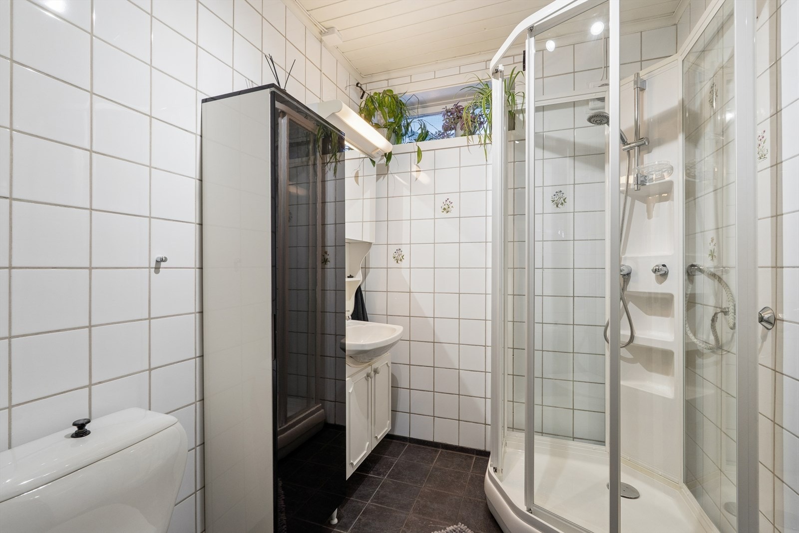 Flislagte vegger og gulv med varmekabler gir et robust bademiljø. Dusjkabinett og servantinnredning kompletterer rommets funksjonalitet. Galleribilde