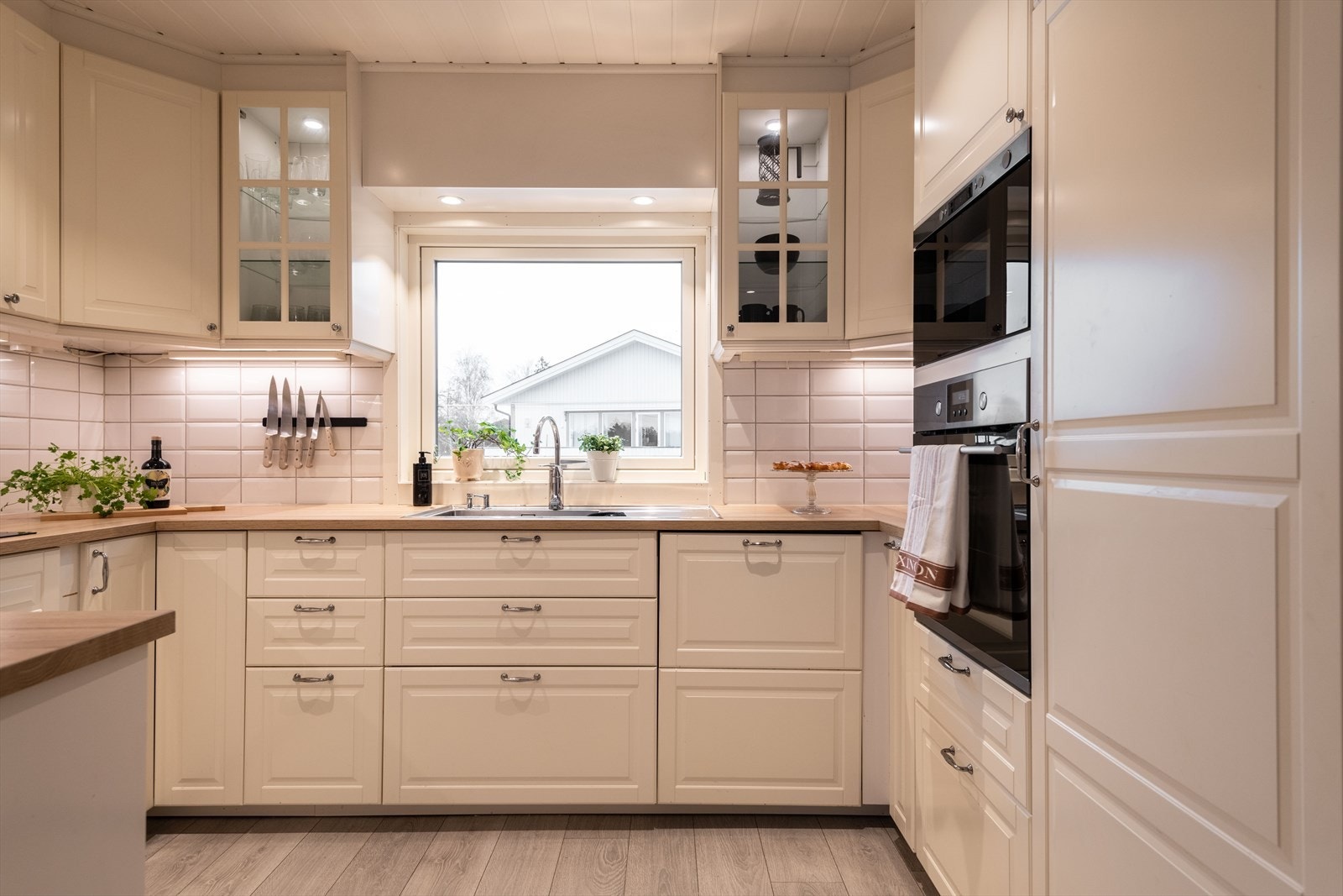 Kjøkkeninnredning med hvite profilerte fronter med og uten glass, med heltre benkeplate med oppvaskkum i stål. Galleribilde