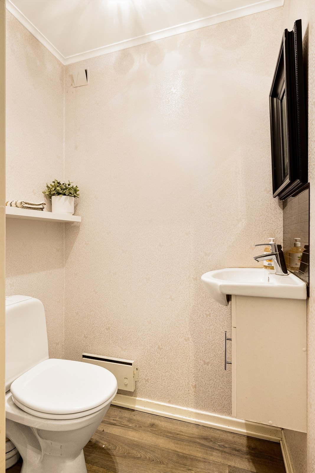 Toalettrom med belegg på gulv og tapet på vegger. Rommet er innredet med klosett, servantskap og veggskap. Galleribilde