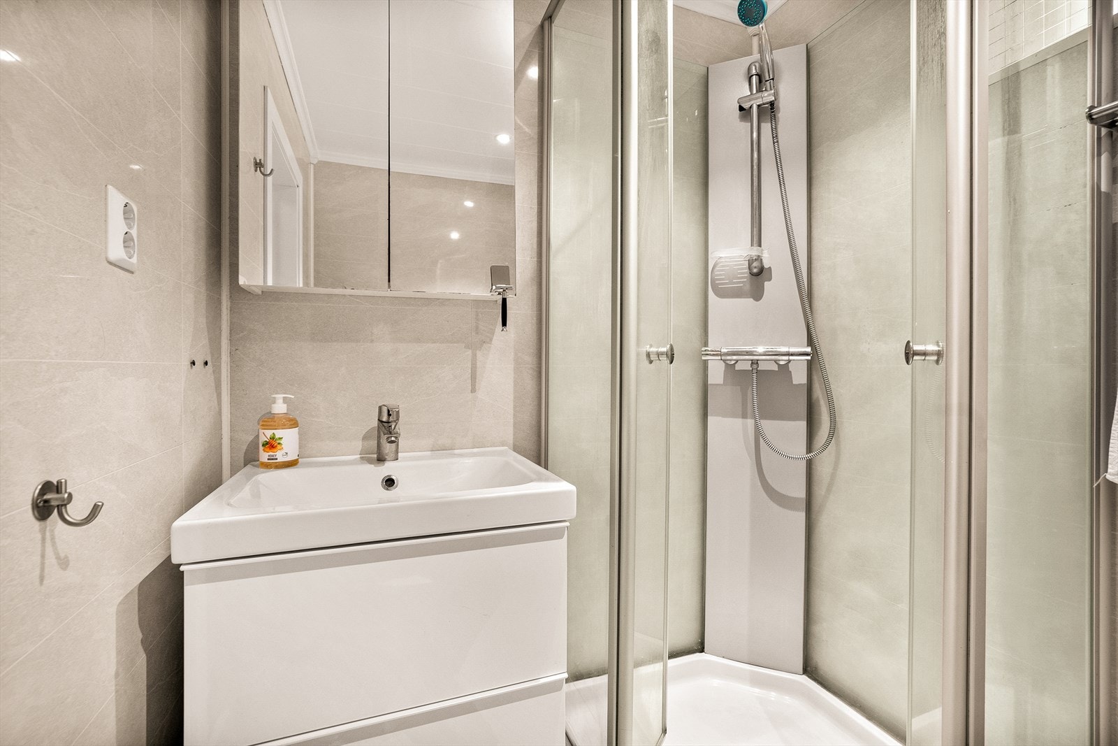 Det er belegg på gulv og vegger med baderomsplater. Rommet er innredet med dusjkabinett, servantskap, speilskap og vegghengt klosett. Galleribilde