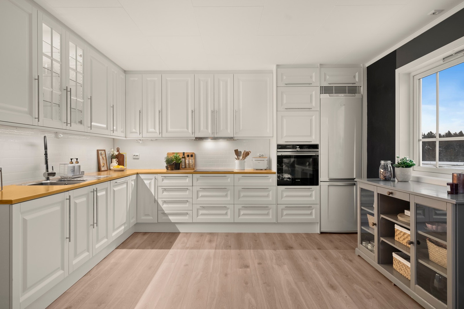 Tidløst og funksjonelt kjøkken med profilerte fronter, gode arbeidsflater og flislagte vegger over benk. Utstyrt med kjøl- og fryseskap, oppvaskmaskin, komfyr og platetopp. Galleribilde