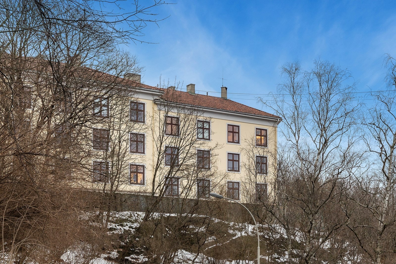 Bygningen er et tre-etasjes leilighetskompleks med loft og kjeller, beliggende i et område med naturlig beplantning. Galleribilde