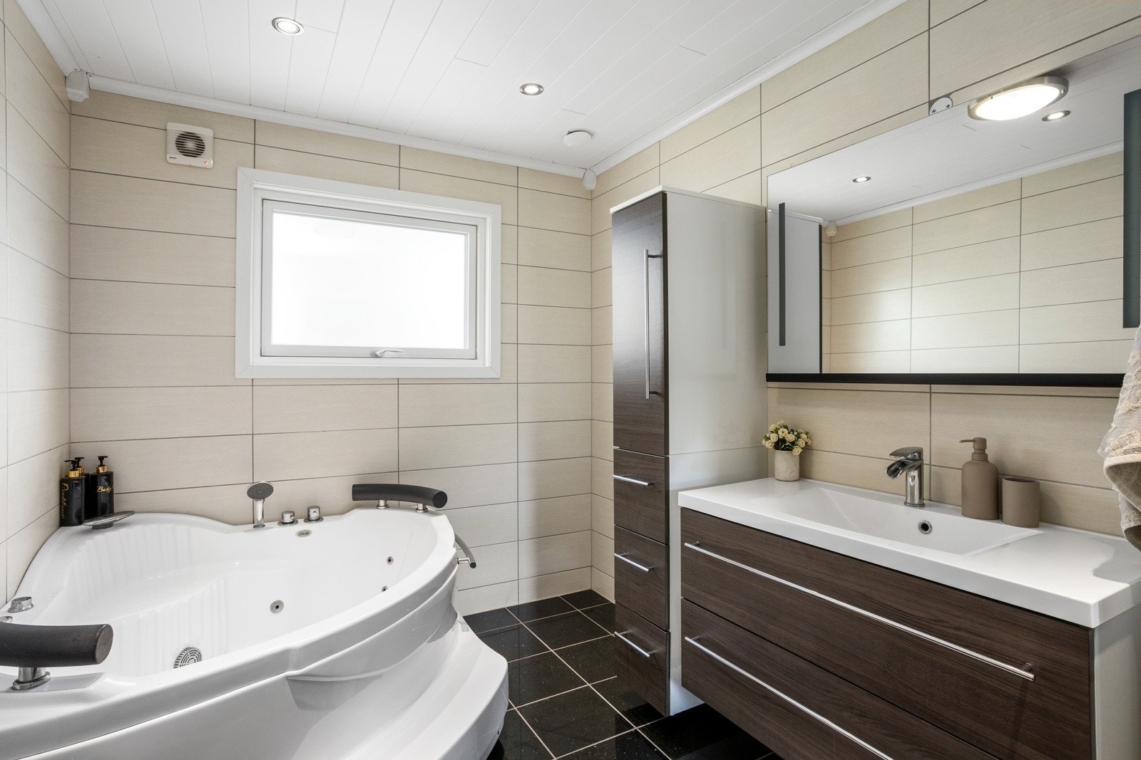 Romslig, flislagt bad med servantinnredning med ekstra oppbevaringsplass og hjørneboblebadekar Galleribilde