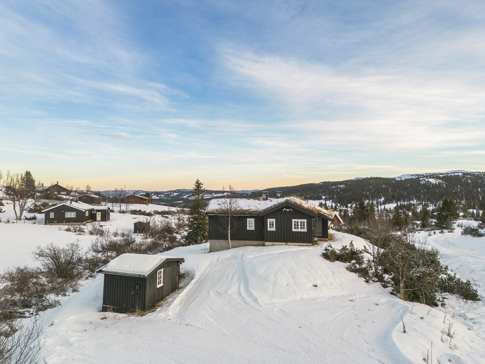 På tunet står et praktisk uthus med to boder - ideelt for lagring av ved, skiutstyr, verktøy og hagemøbler. På yttervegg er det montert elbillader. Galleribilde