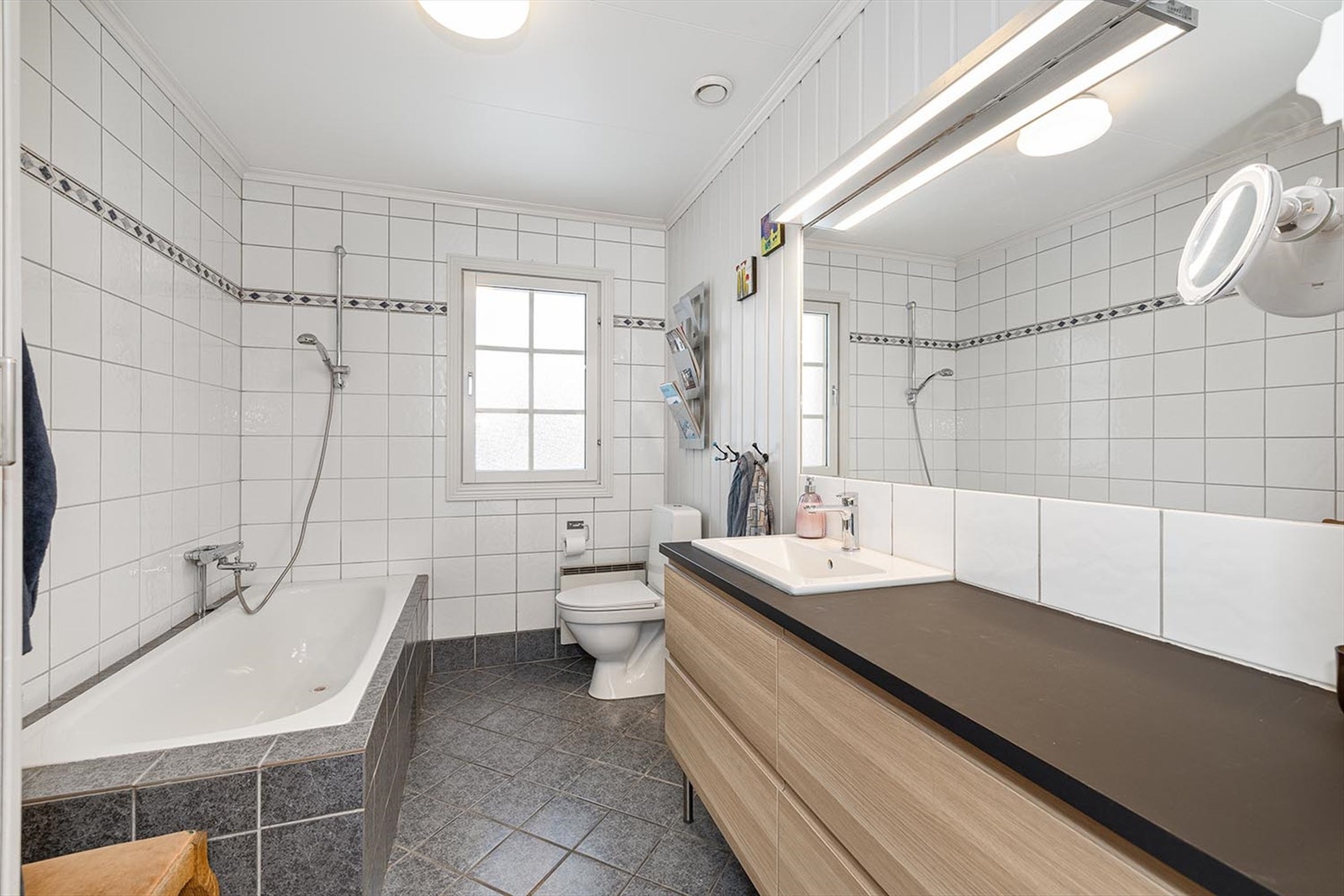 Flislagt bad med gode oppbevaringsmuligheter. Her finner du et badekar, toalett og servant med oppbevaringsmuligheter. Galleribilde