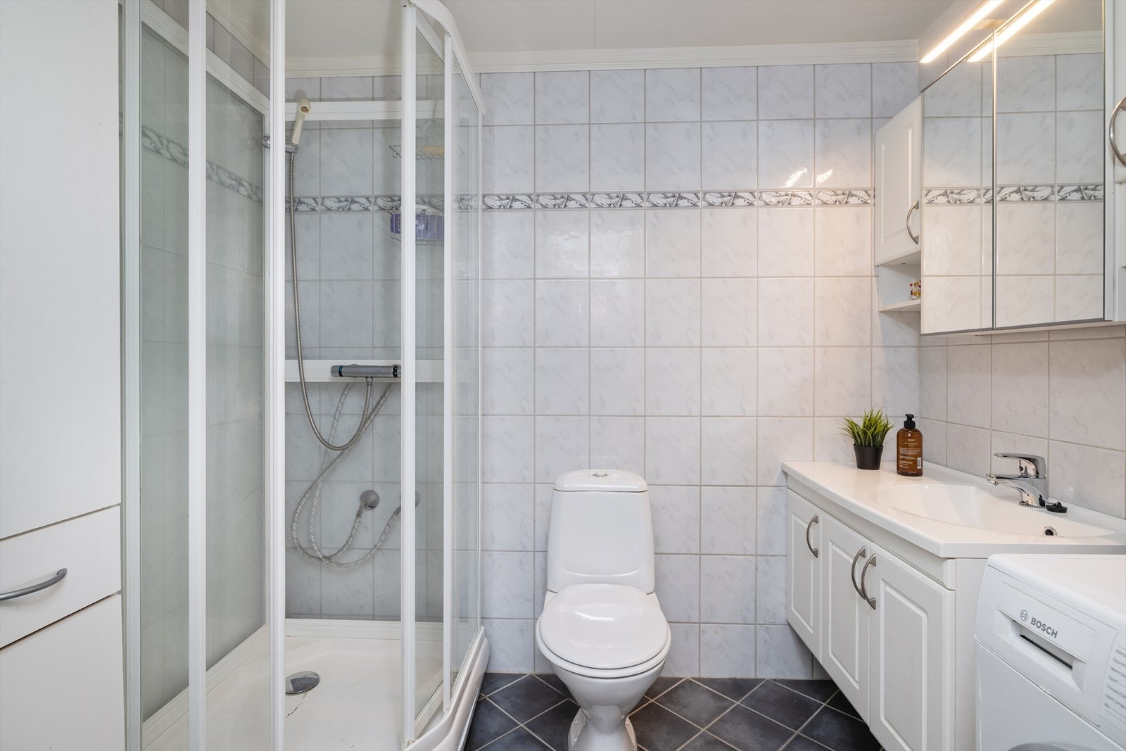 Flislagt bad og wc med innholdsrik baderomsinnredning i hvitt Galleribilde