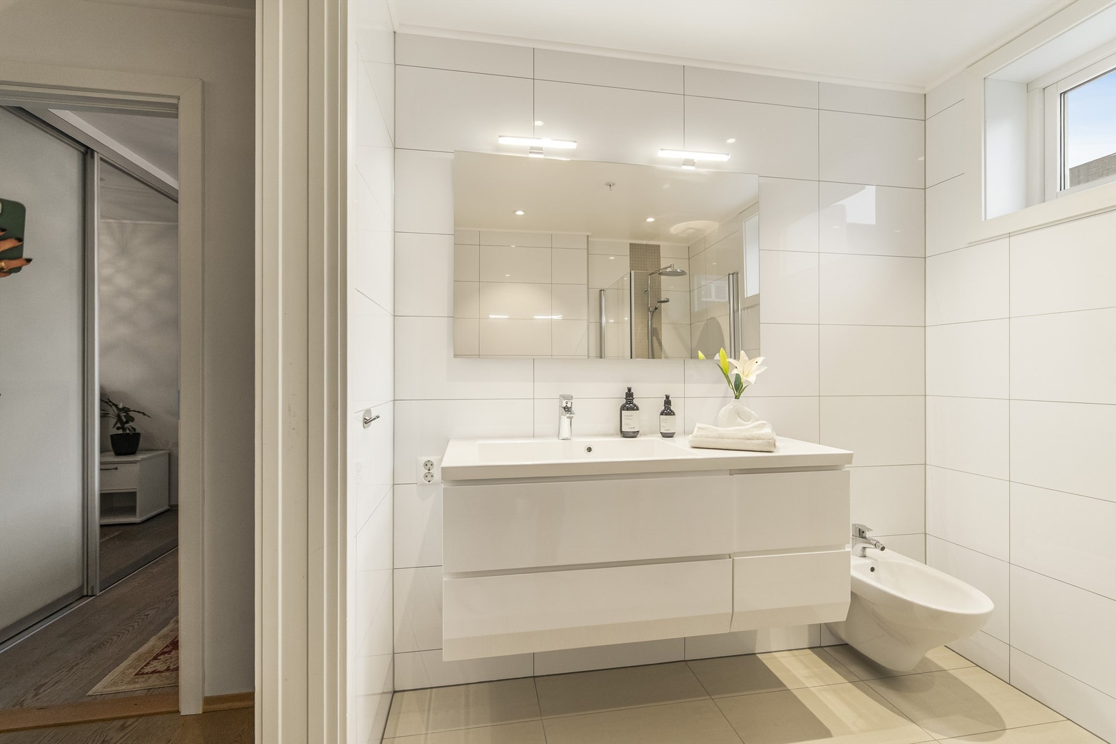 Badet er innredet med dusjhjørne, bidè, vegghengt toalett og servant i innredning Galleribilde