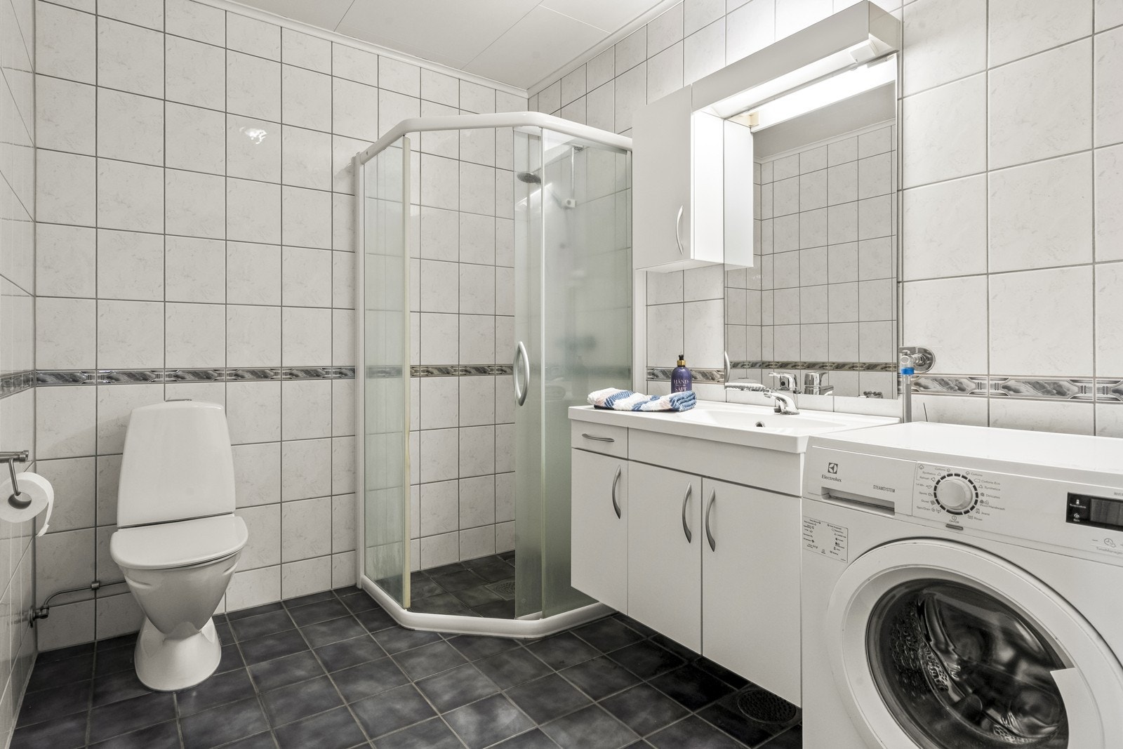 Flislagt bad med dusjhjørne og opplegg for vaskemaskin. Galleribilde