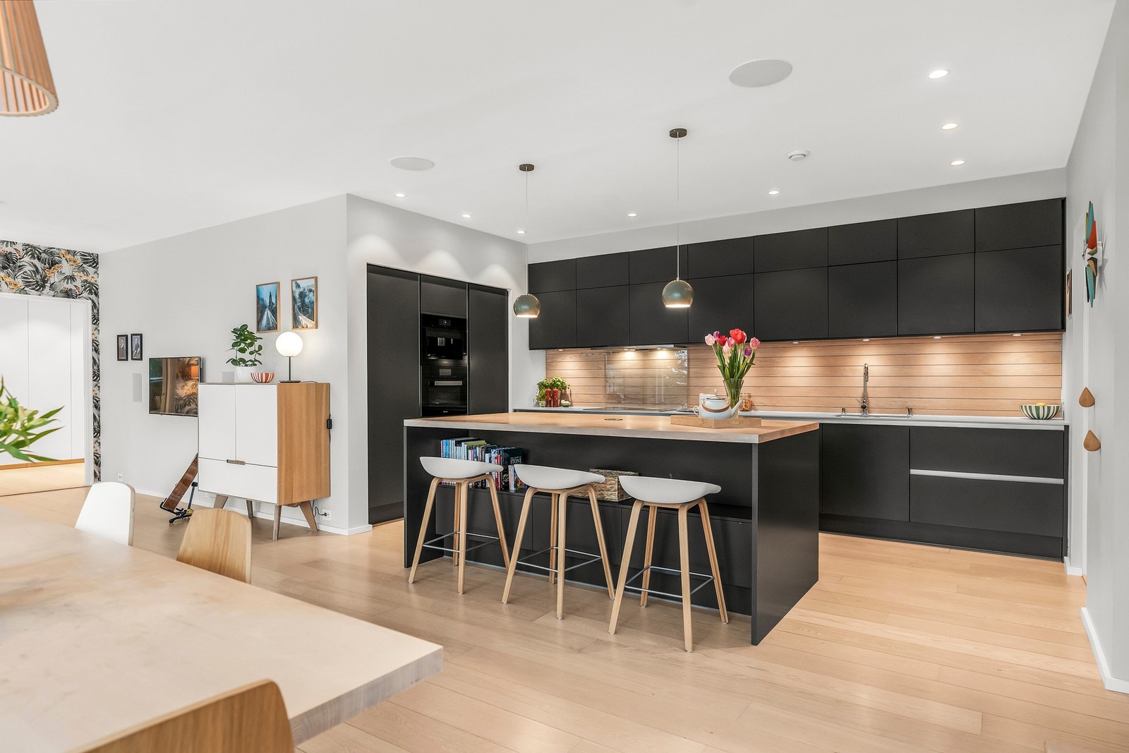 Moderne kjøkken fra HTH med åpen løsning, pent gulv og mørke skapinnredninger. Integrerte hvitevarer og praktisk kjøkkenøy med sitteplasser. Galleribilde
