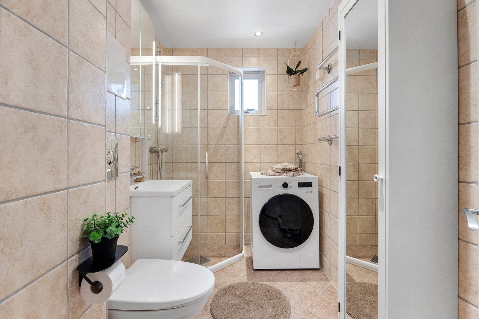 Badet er innredet med enkel servant med skuffer, speilskap med belysning, vegghengttoalett, høyskap, dusjvegger og opplegg for vaskemaskin Galleribilde