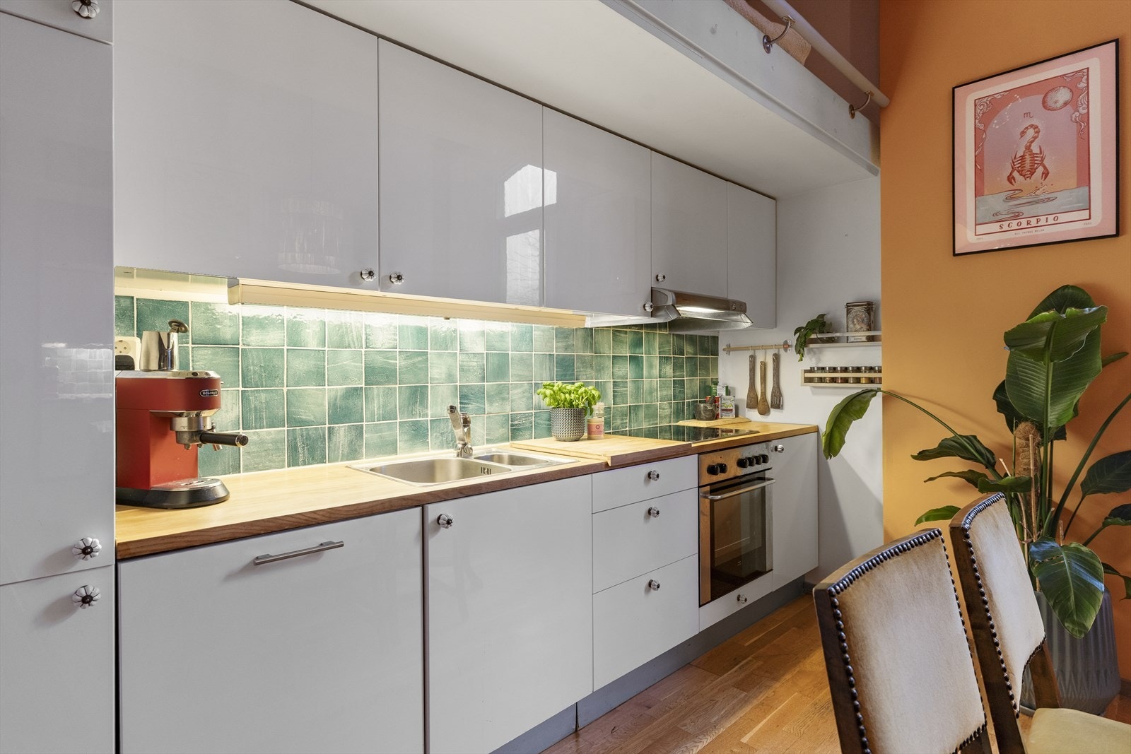 Kjøkkeninnredningen har glatte høyglans hvite fronter og heltre benkeplate i eik med nedfelt rustfri oppvaskkum og ettgreps blandebatteri. Det er montert belysning under overskap samt flislagt vegg over benk, utført i 2021 Galleribilde