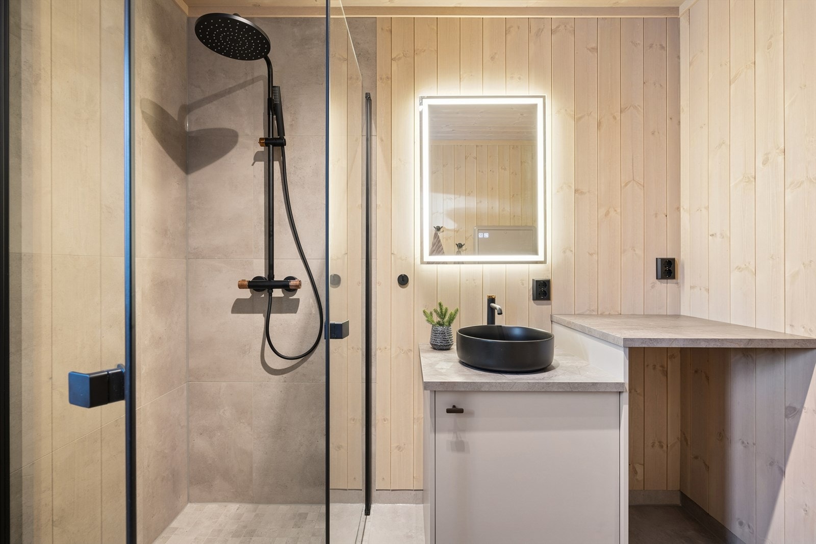 Badet inneholder vegghengt toalett, dusjhjørne med glassdører, servant med innredning og opplegg for vaskemaskin. Galleribilde