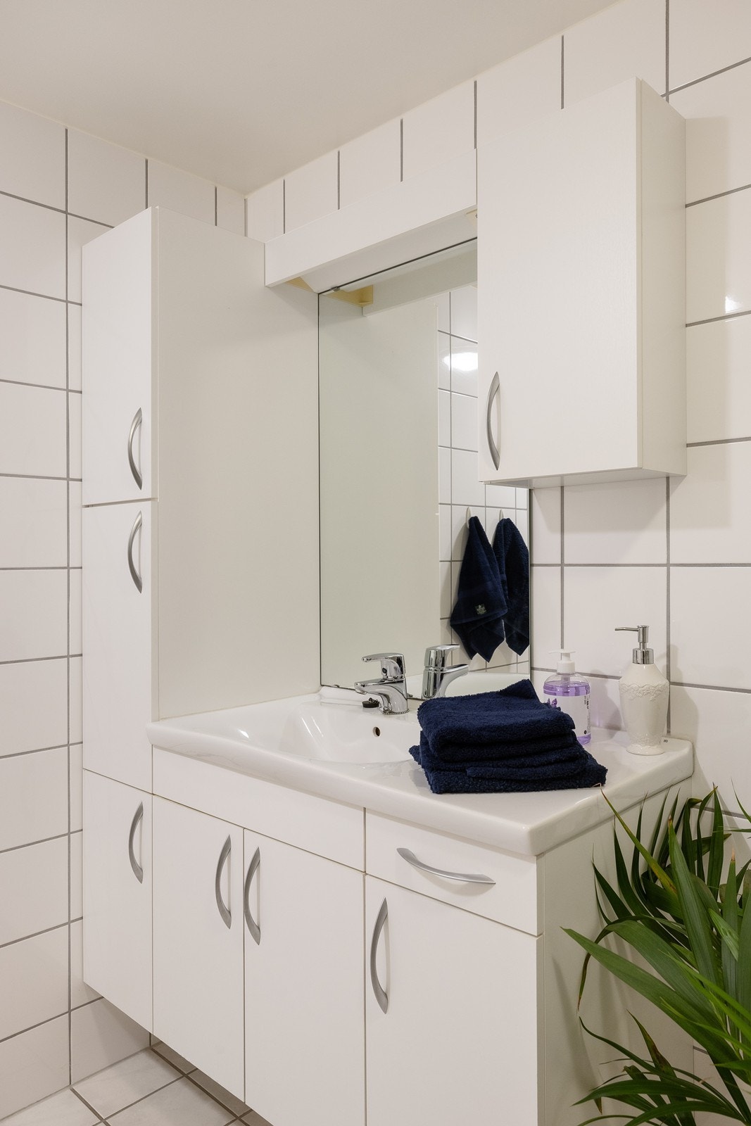 Innredningen har heldekkende servant over skapseksjon i hvitt, matchende veggskap og speil med belysning. Galleribilde