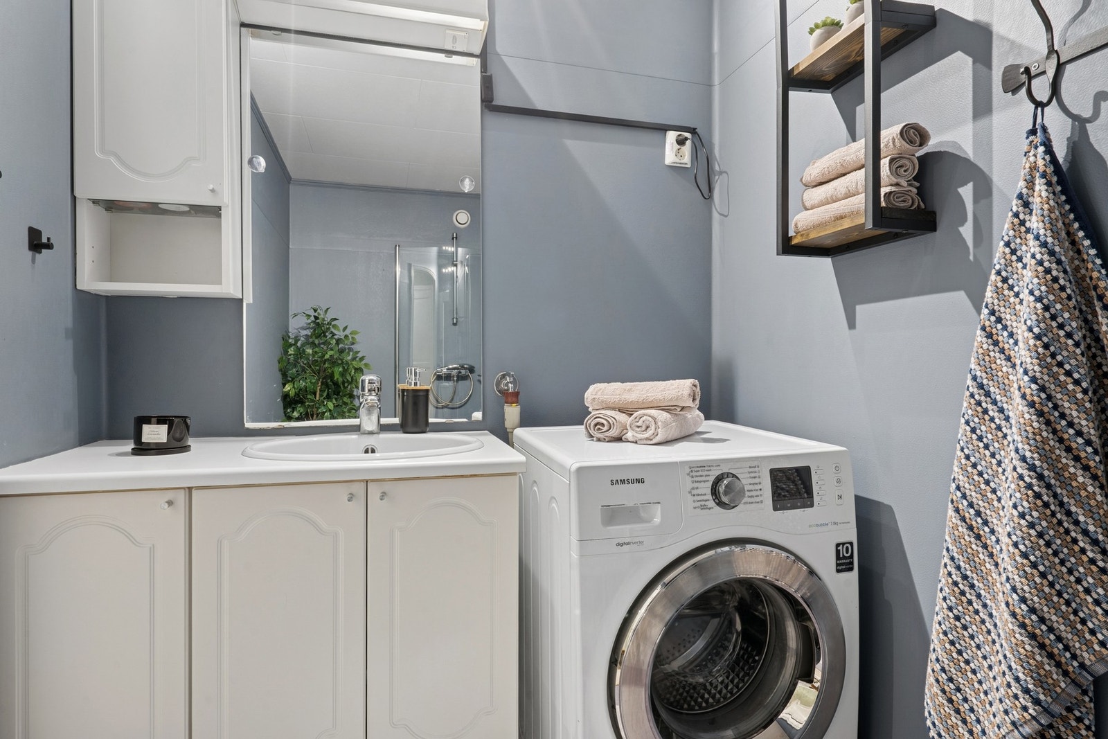 Frittstående toalett. Dusjhjørne med buede dører og ett-greps armatur med hånddusj. Opplegg for vaskemaskin og dobbel stikkontakt på vegg. Galleribilde