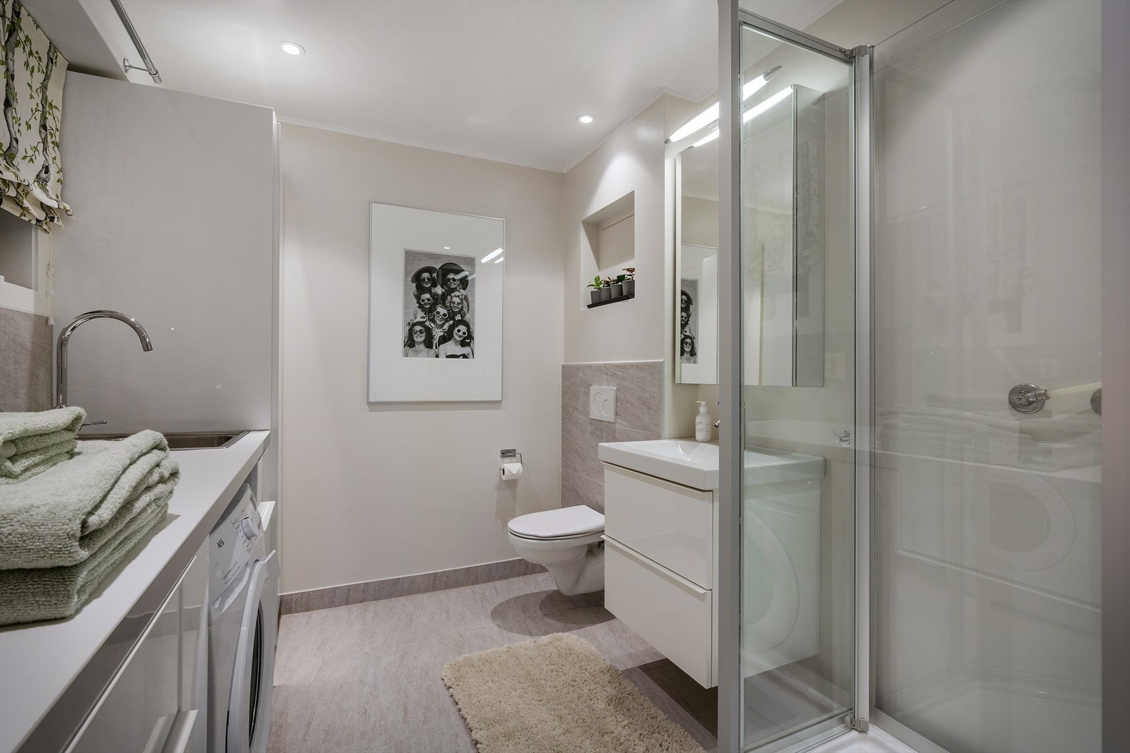 Badet er innredet med dusjkabinett, nedsenket servant, utslagsvask, opplegg til vaskemaskin og vegghengt toalett. Galleribilde