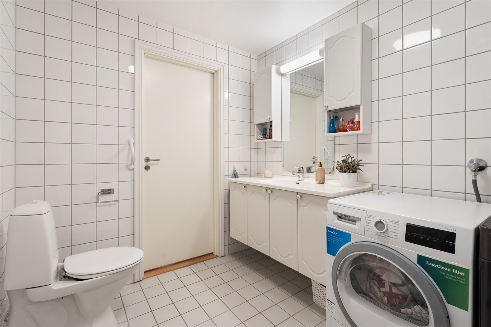 Badet har innredning med nedfelt servant, toalett, dusjvegger/hjørne og opplegg for vaskemaskin. Galleribilde