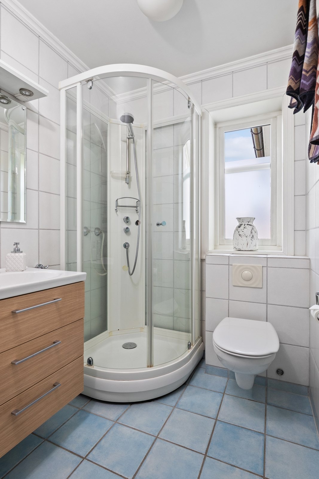 Badet nede er innredet med hvite veggfliser og lyseblå fliser på gulvet. Galleribilde