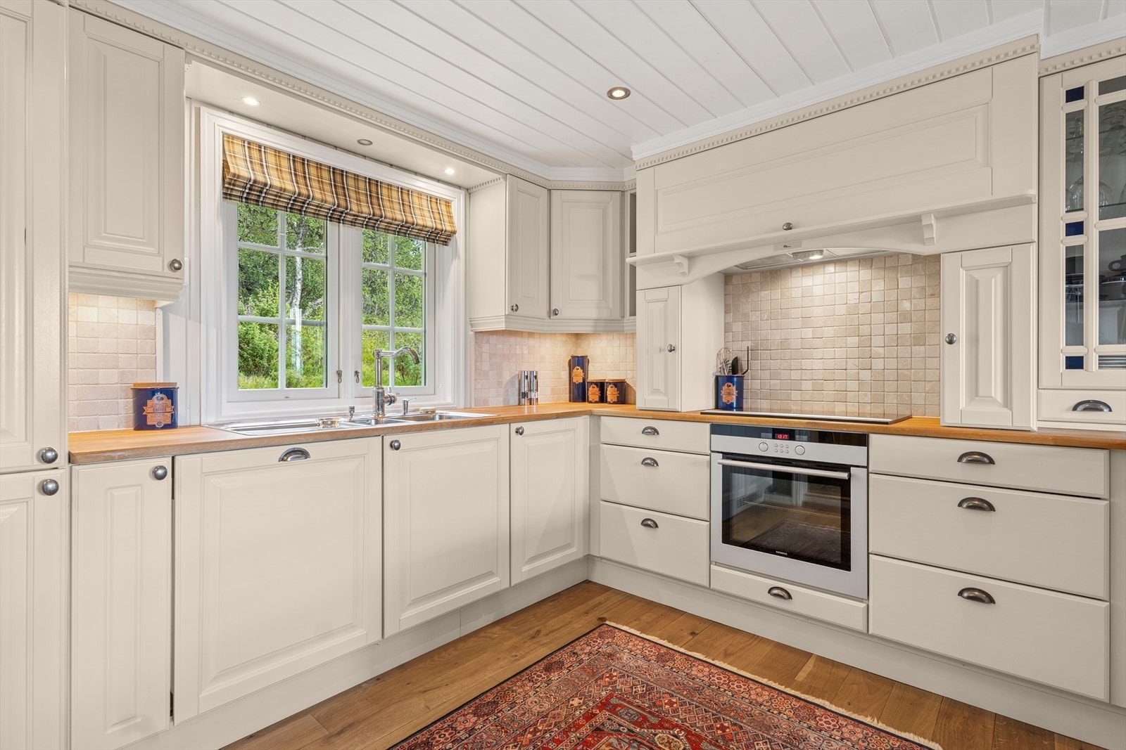 Heltre kjøkkeninnredning med malte fronter, overskap til himling, spotter i lyskasse over vindu/oppvaskkum og skuffer med selvinntrekk/demping. Benkeplaten er i heltre eik med nedfelt oppvaskkum og en 70 cm bred induksjonstopp med 4 kokesoner. Galleribilde