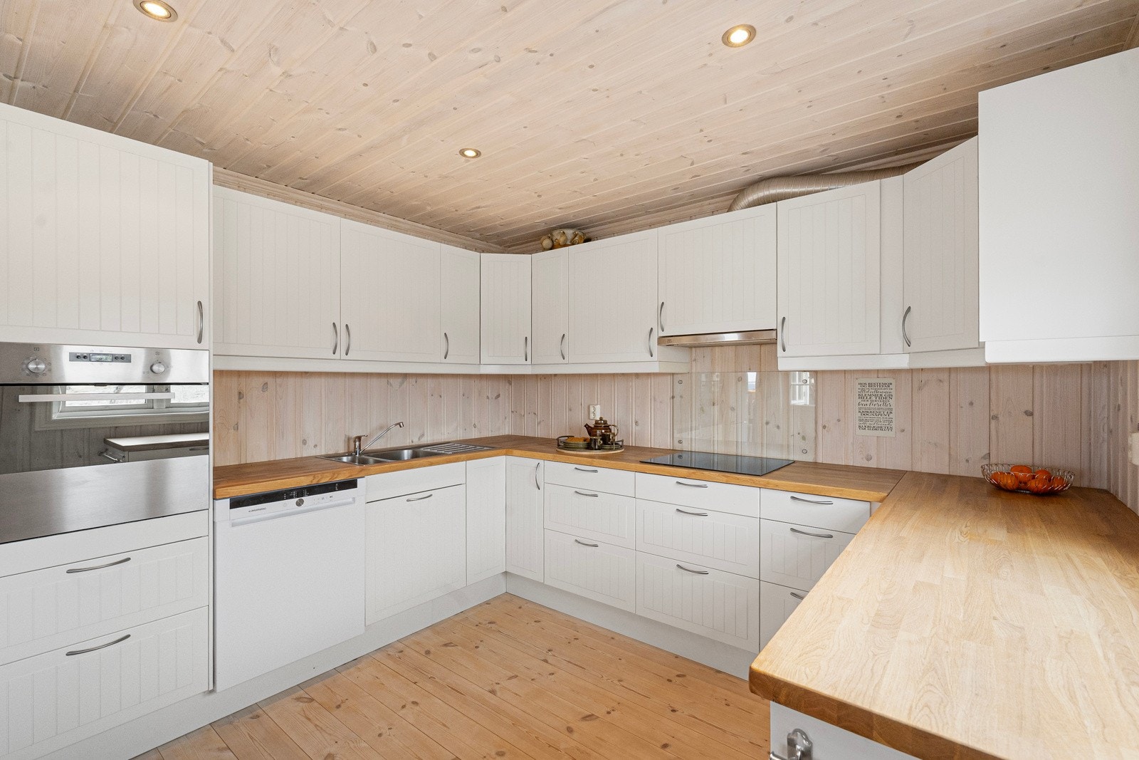 Heltre benkeplate med nedfelt vask og platetopp, samt integrerte hvitevarer som oppvaskmaskin, stekeovn og kjøleskap Galleribilde