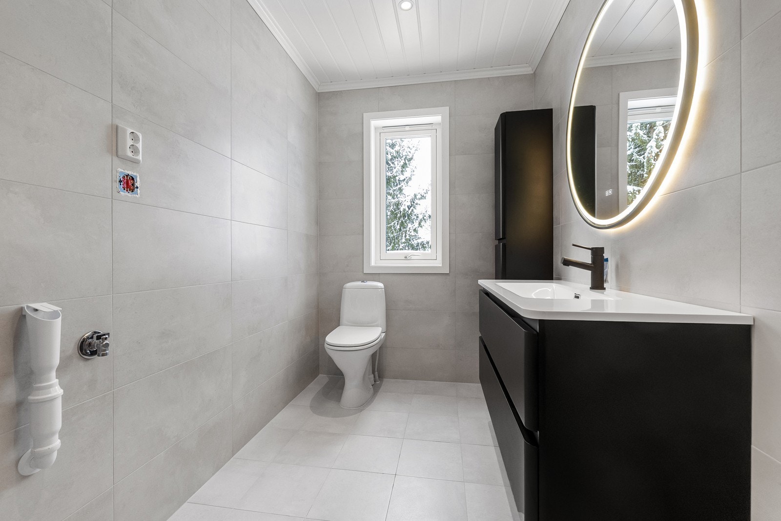 Nyoppusset bad fra 2025 med flislagt gulv med gulvvarme. Utstyrt med et frittstående toalett, servant i baderomsinnredning, opplegg for vaskemaskin og plass til tørketrommel. Galleribilde