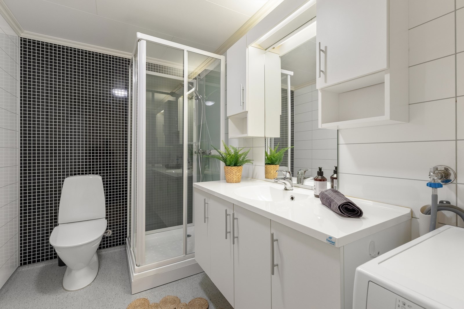 Her er det opplegg for vaskemaskin, innredning med benkeskåp, støypt servant, overskåp og spegel med lyslist, dusjkabinett og toalett. Galleribilde