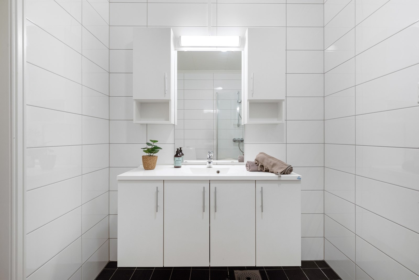 Badet har tidlaus innreiing med kvite og glatte underskåp og overskåp, støypt servant, lyslist og spegel, toalett og dusjveggar. Galleribilde