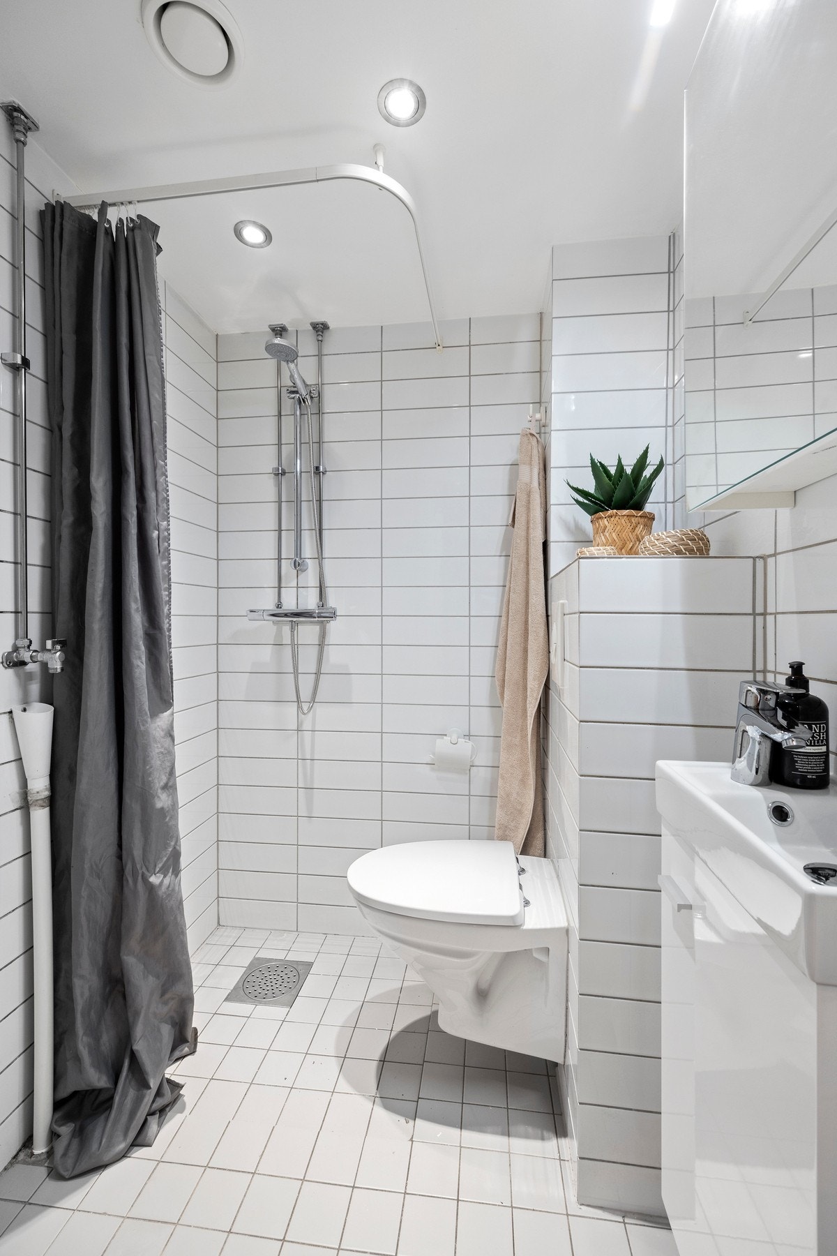 Flislagt baderom med vegghengt wc, dusjhjørne, servantskap med overhengende speilskap og belysning. Opplegg for vaskemaskin. Galleribilde