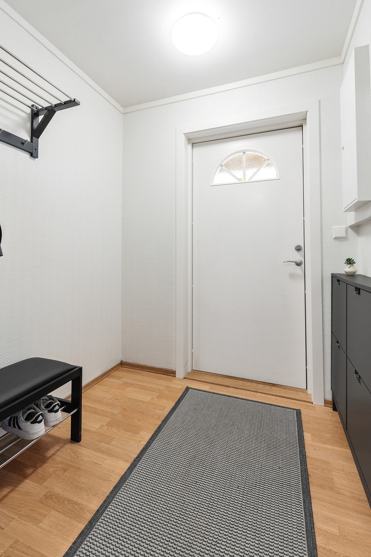 Romslig entré med parkett på gulv, malt tapet på vegger og slett flate i himling. Det er plass til oppheng av yttertøy og sko Galleribilde