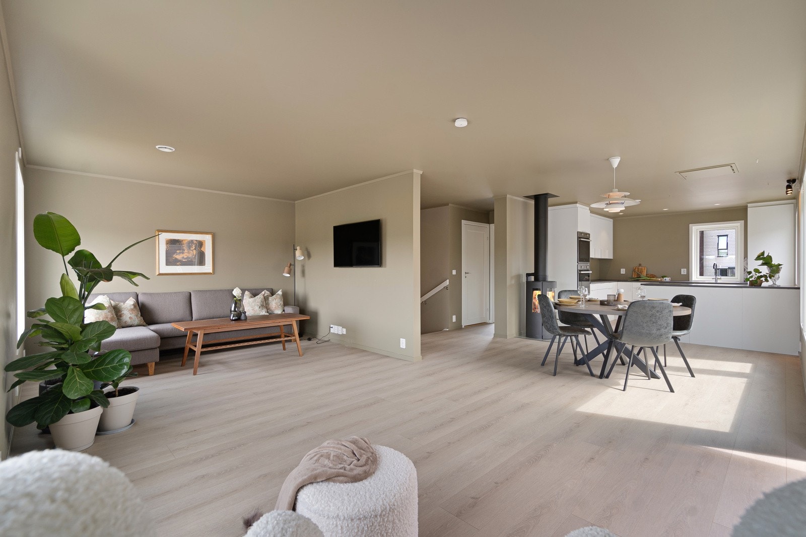 Den åpne løsningen mot kjøkkenet skaper en sosial atmosfære, perfekt for både hverdag og selskap. Her er det god plass til sofagruppe og spisebord, og vedovnen gir lun varme og en koselig stemning på kjølige kvelder. Galleribilde