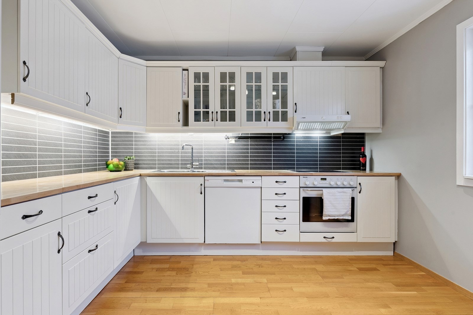 Kjøkkeninnredning med profilerte fronter, rikelig skapplass og god arbeidsbelysning under overskapene. Galleribilde