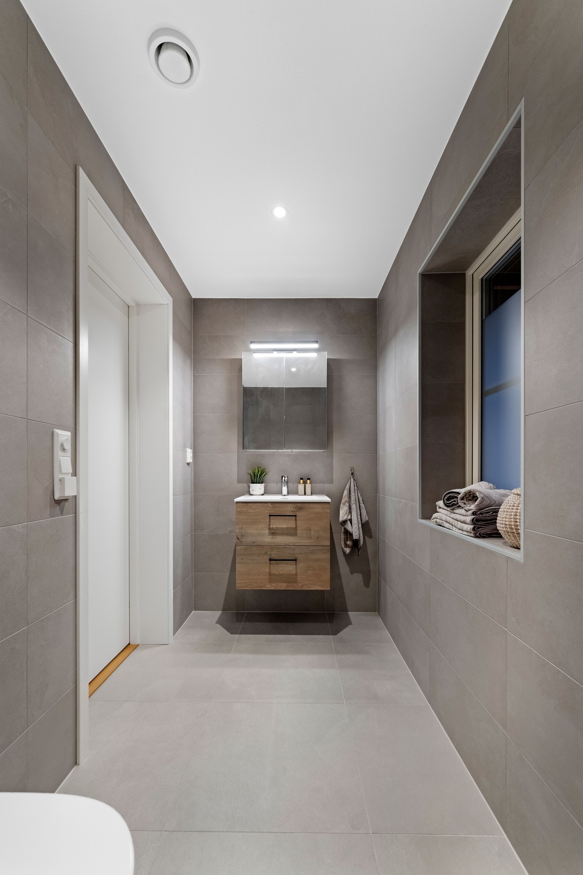 Boligens toalettrom i første etasje har adkomst fra stue/kjøkken området. Her får man fliser på både gulv og vegger, himling med slette overflater, og en lekker innredning med glatte fronter. Galleribilde