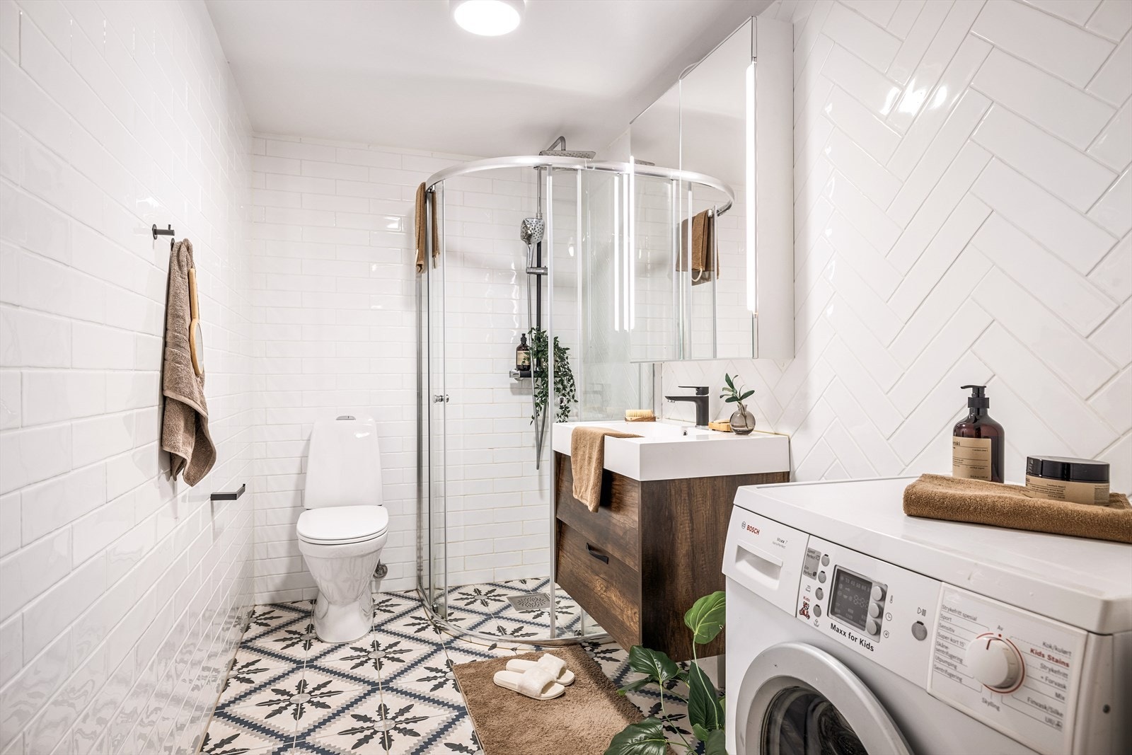 Badet er innredet med dushjørne med dører av glass, klosett, møblement med servant og overskap med speilfelt med integrert lys, samt opplegg for vaskemaskin. Galleribilde