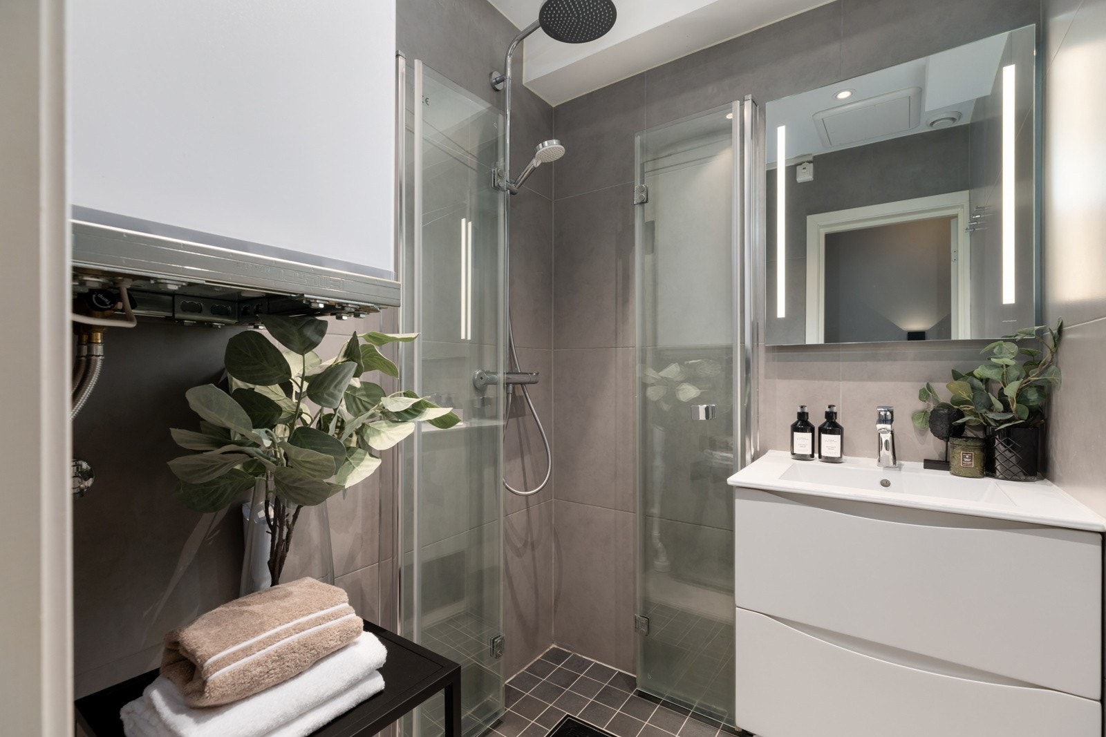 Leiligheten har et dusjbad og et separat toalettrom. Badet ble rehabilitert i 2023 og har en moderne standard. Rommet er utført med gråbeige storformatfliser på veggene, matchende fliser i 40 x 60 på gulvet og mørkere, mindre fliser på gulvet i dusjsonen. Galleribilde