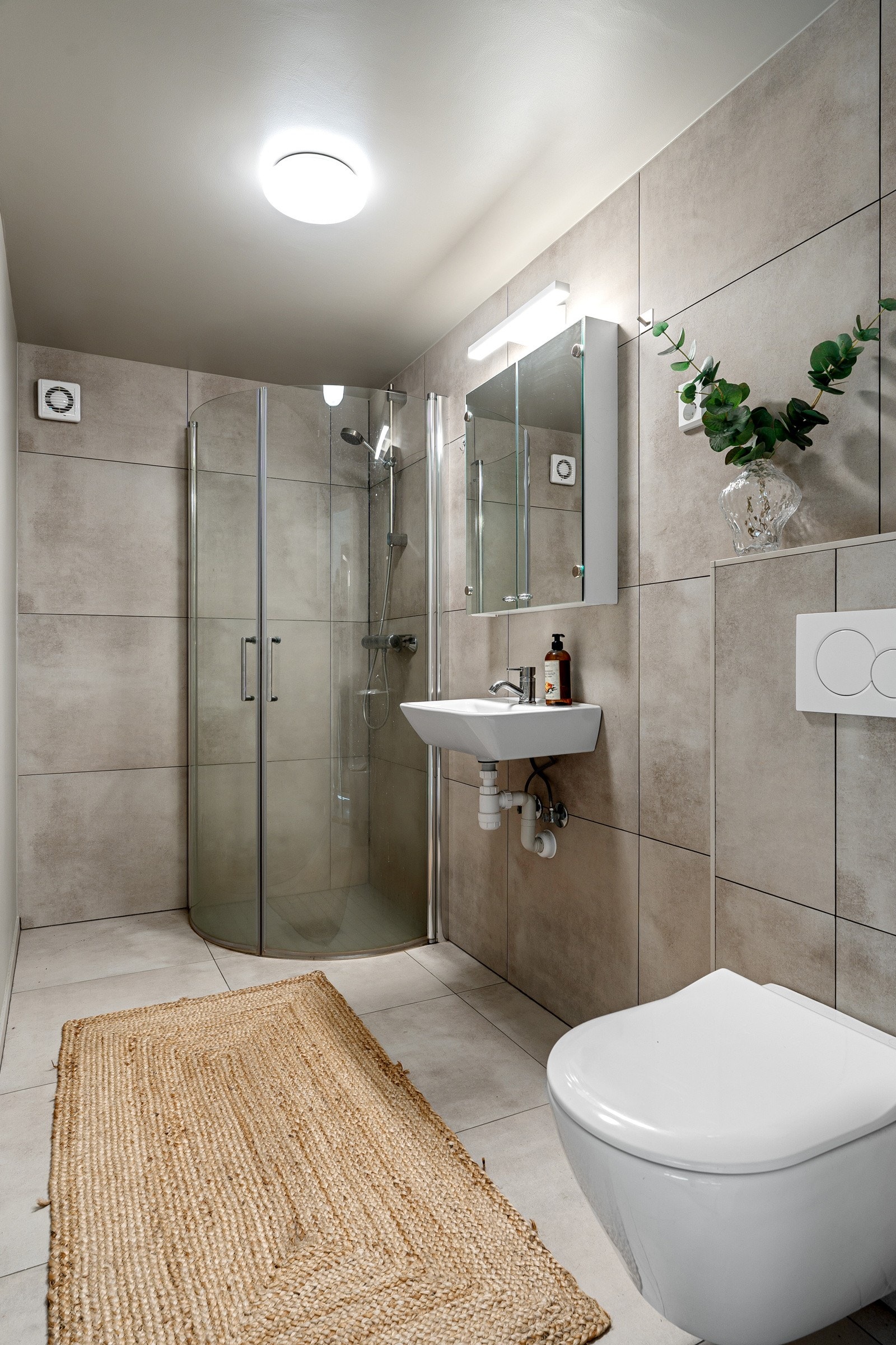 Innbydende baderom med fliser i vegg og gulv, behagelig gulvvarme. Av utstyr finnes innredning med servant, dusjvegger av glass og dusjgarnityr på vegg.