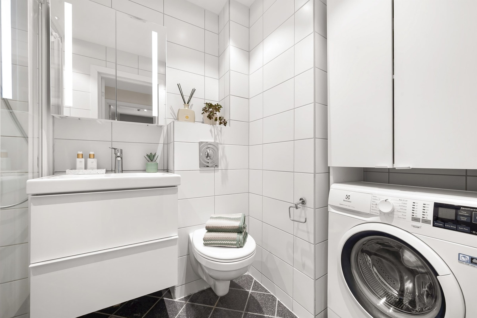 Pent flislagt bad/WC med vegghengt toalett, speil overskap og nyere vask med skuffeskap. Vaskemaskin og skap over medfølger. Galleribilde